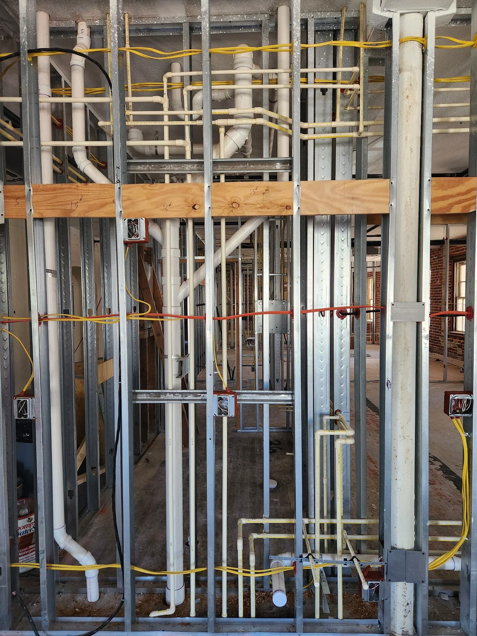 Construction framing with exposed metal studs, electrical wiring, and plumbing pipes in a building under construction.