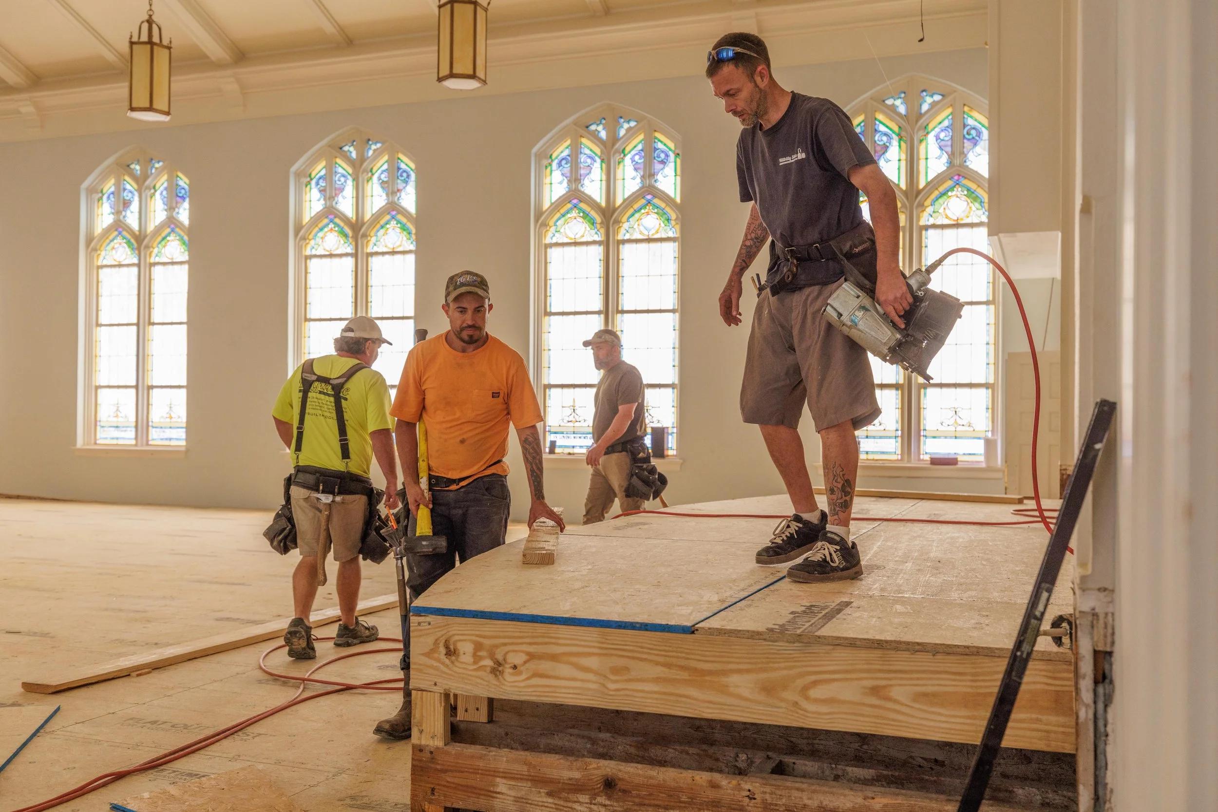 Workers installing wooden flooring or stage in a large church hall with stained glass windows.