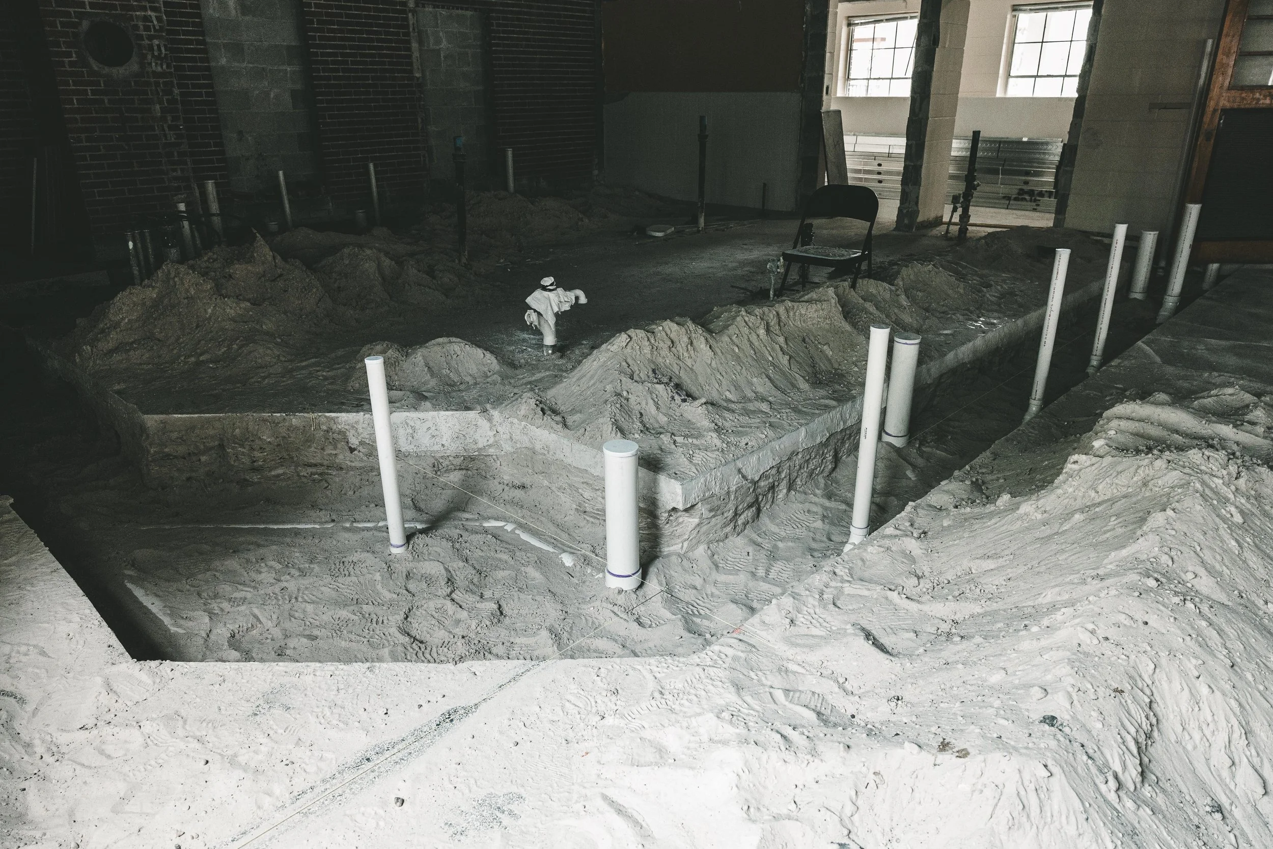 Construction site inside a building with dirt piles, PVC pipes, and a plastic figurine of a construction worker.