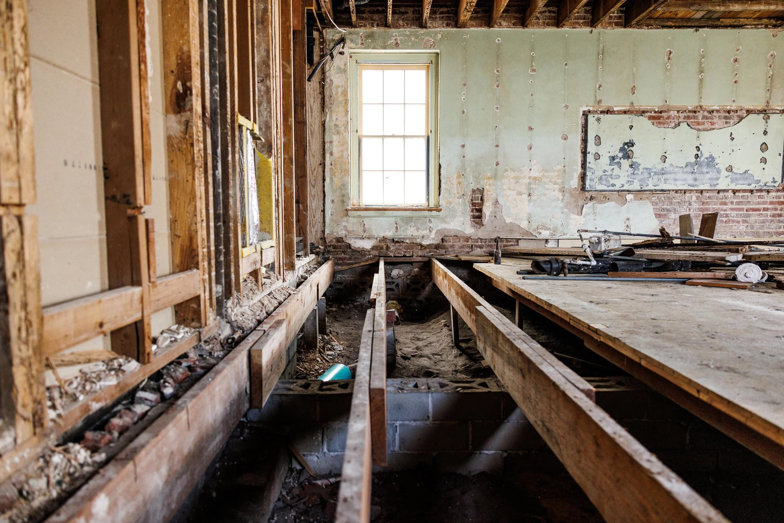 Interior of a house under renovation with exposed wooden framing, a window, and a partially demolished wall.