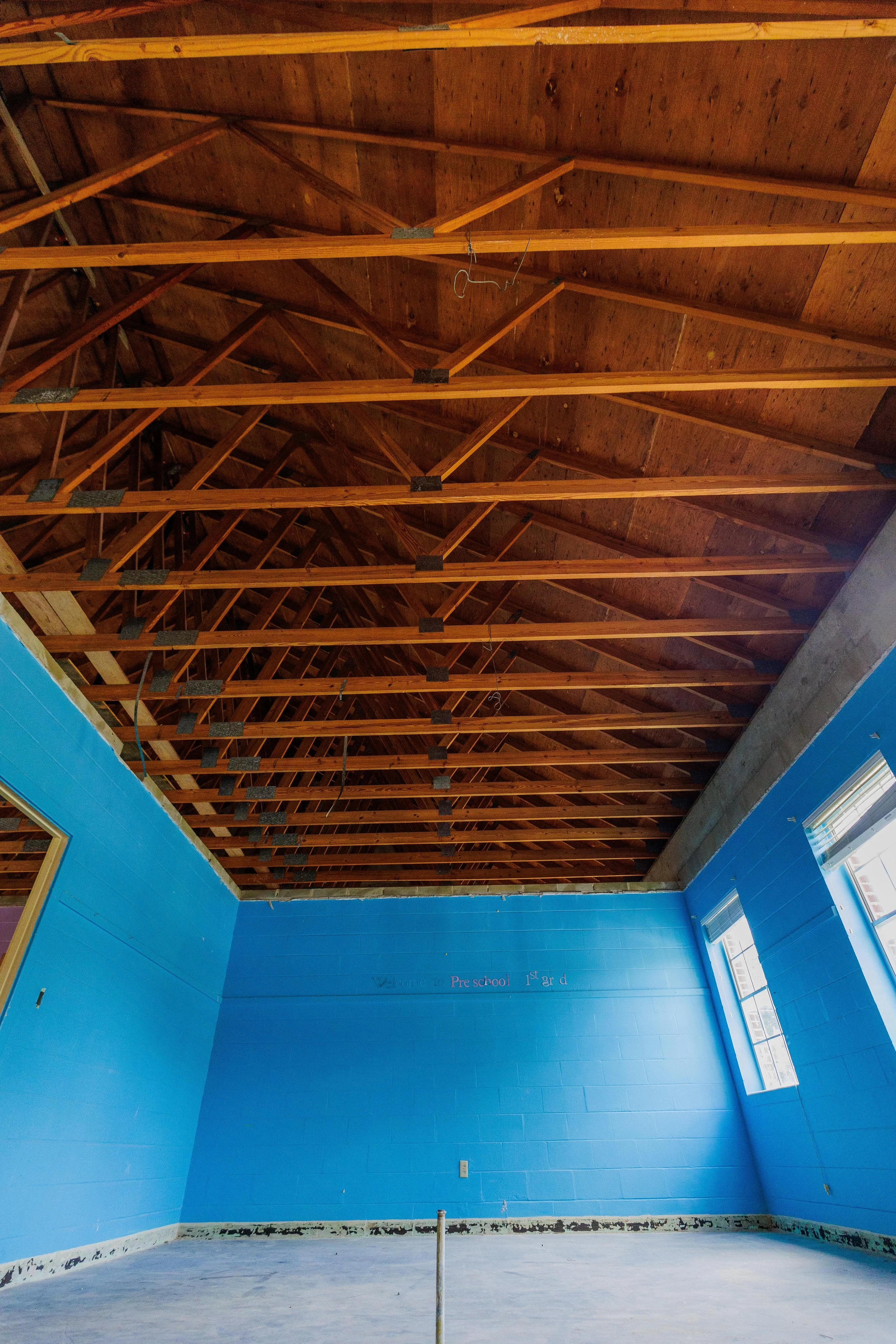 Interior of a classroom with exposed wooden ceiling beams, blue-painted walls, and windows letting in natural light.
