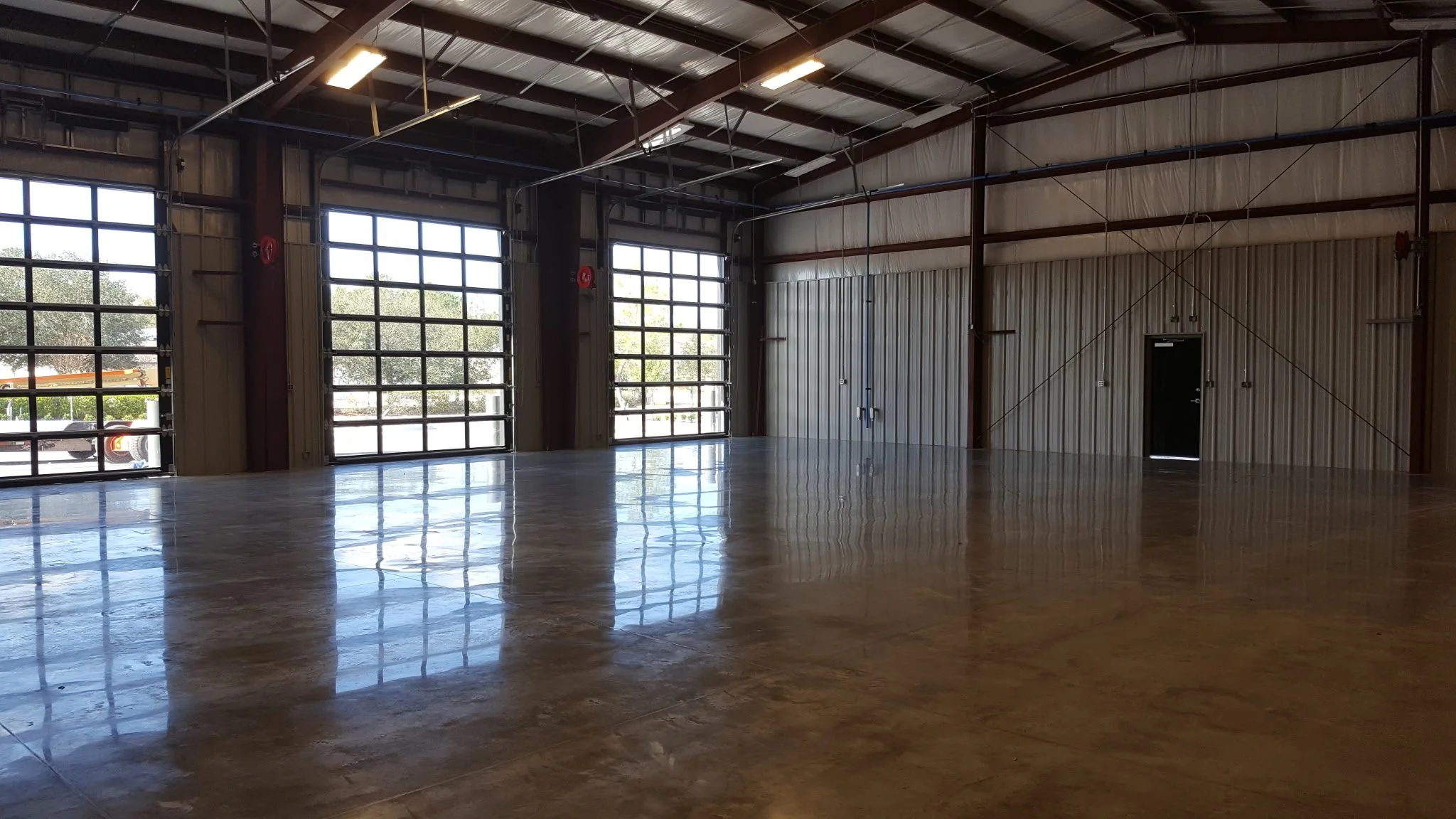 Empty industrial warehouse with polished concrete floor, large roll-up doors, and metal walls and ceiling.
