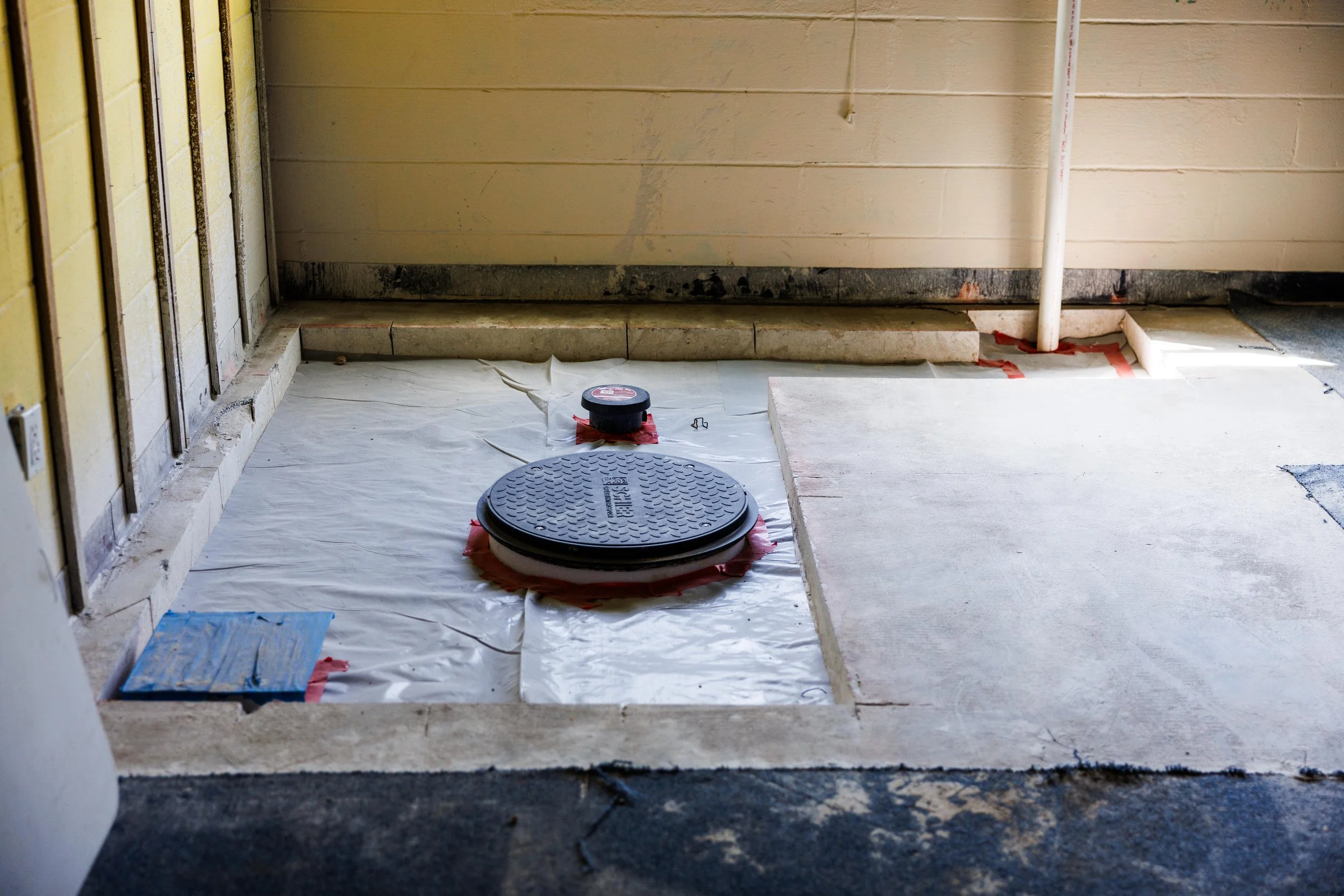 Bathroom renovation in progress with a new toilet flange installed on a partially tiled floor, covered with protective paper and tape.