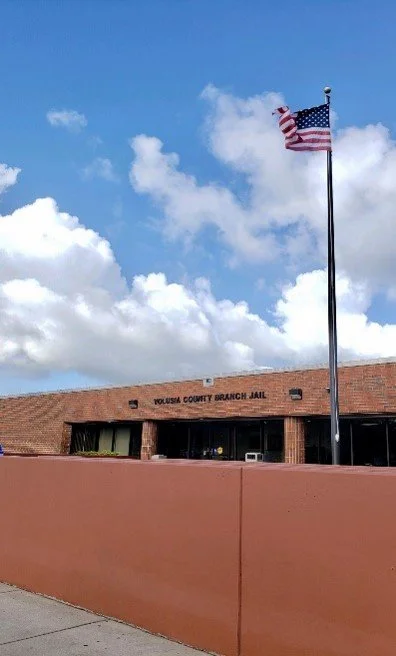 American flag flying outside the Tulsa County Branch Jail building under a partly cloudy sky.