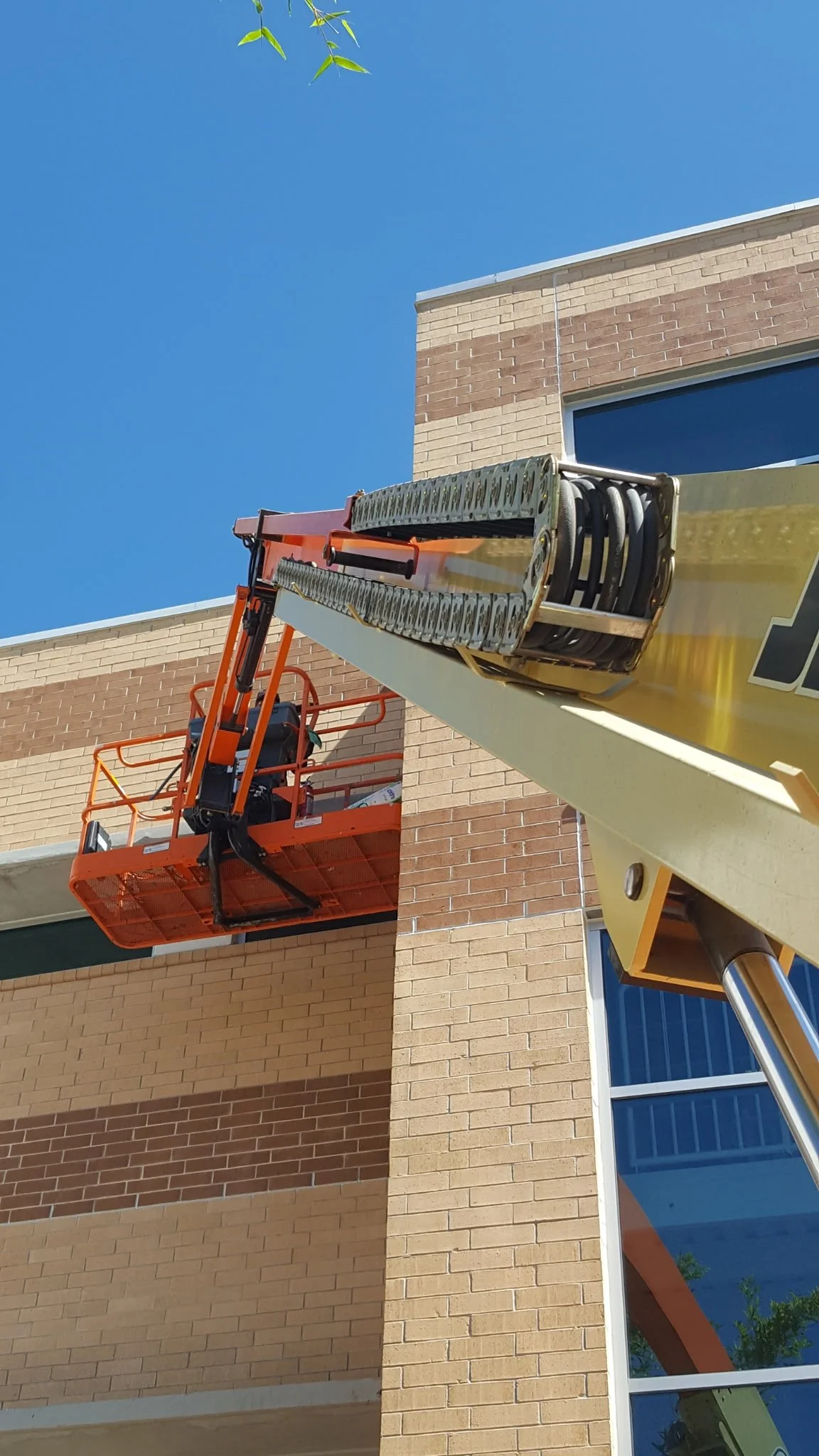 A paint lift platform extended next to a brick building with large windows, blue sky in the background.