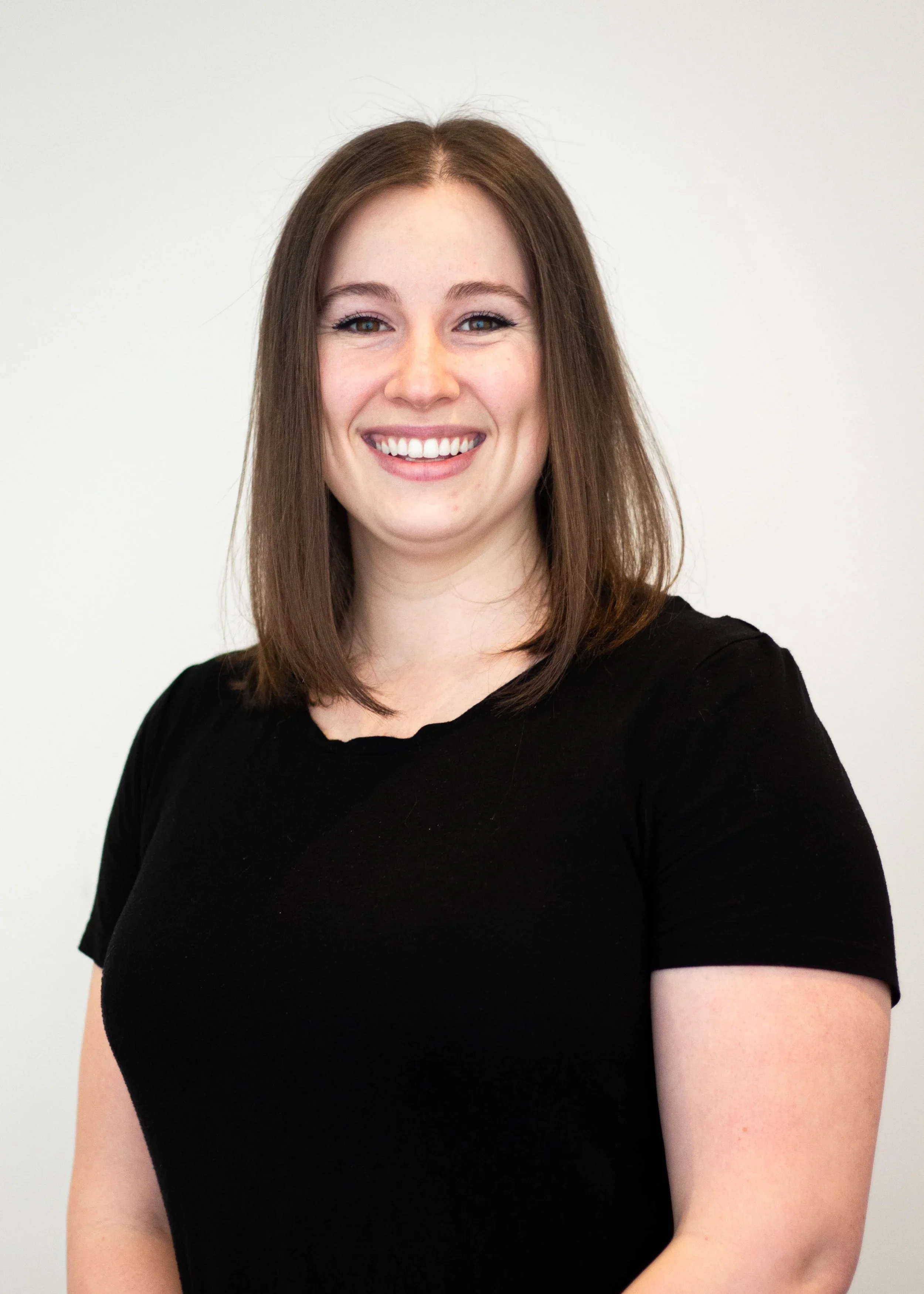 Holly is an RMT at Golden Ember. A smiling woman with shoulder-length brown hair, wearing a black top, standing against a plain light-colored background.