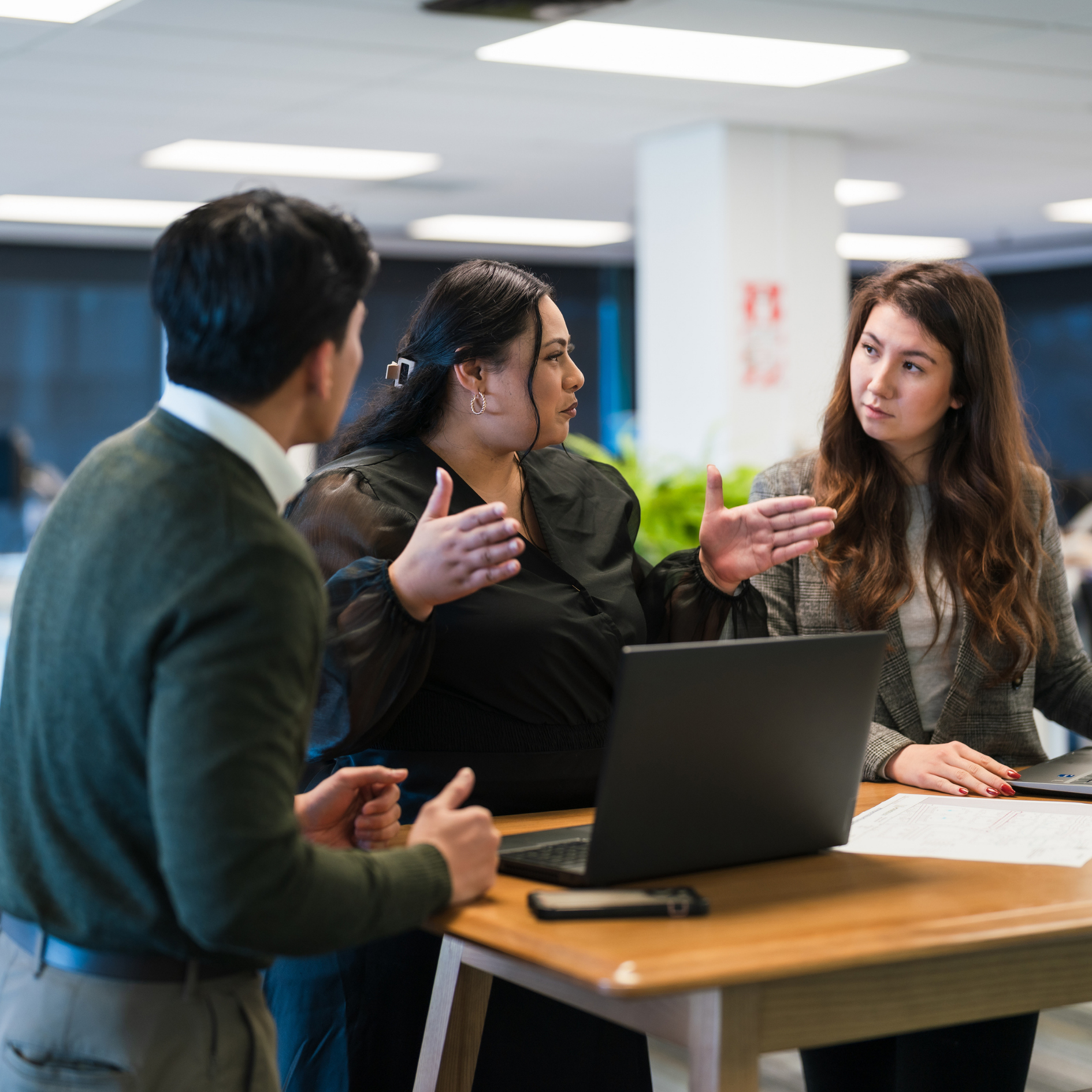 Three professionals collaborating at a table in an office, discussing joint commission.
