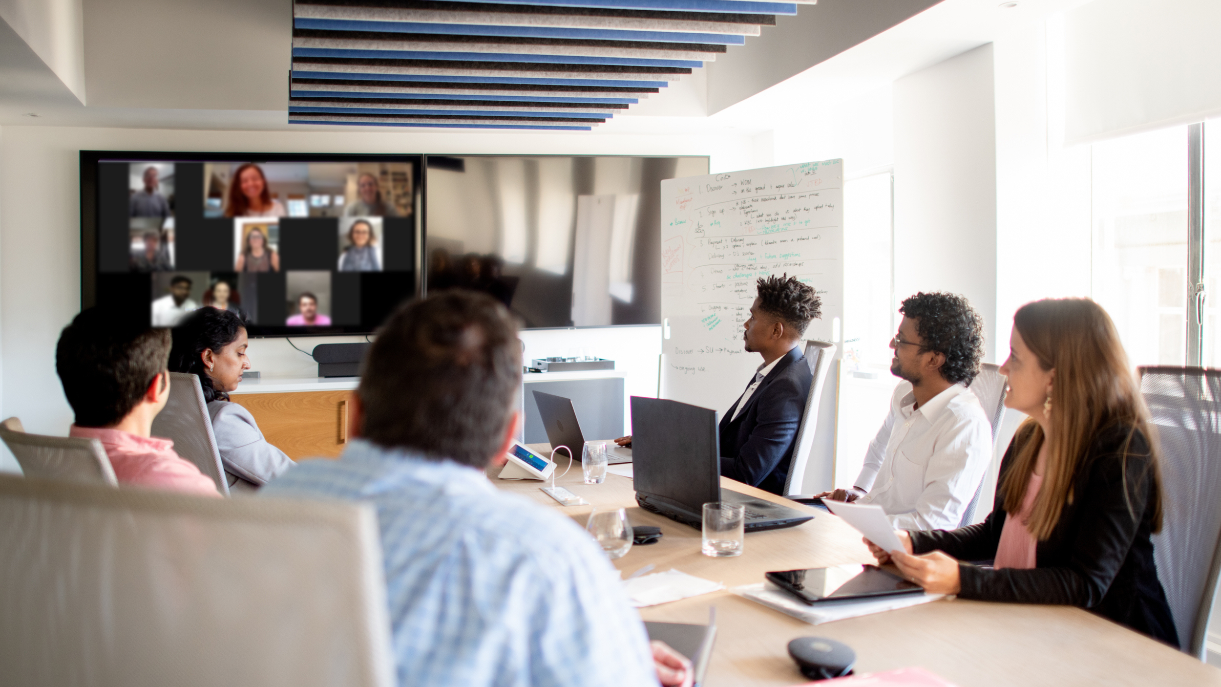 Group of healthcare compliance consulting professionals seated around a conference table in an office, participating in a hybrid meeting about accreditation consulting.