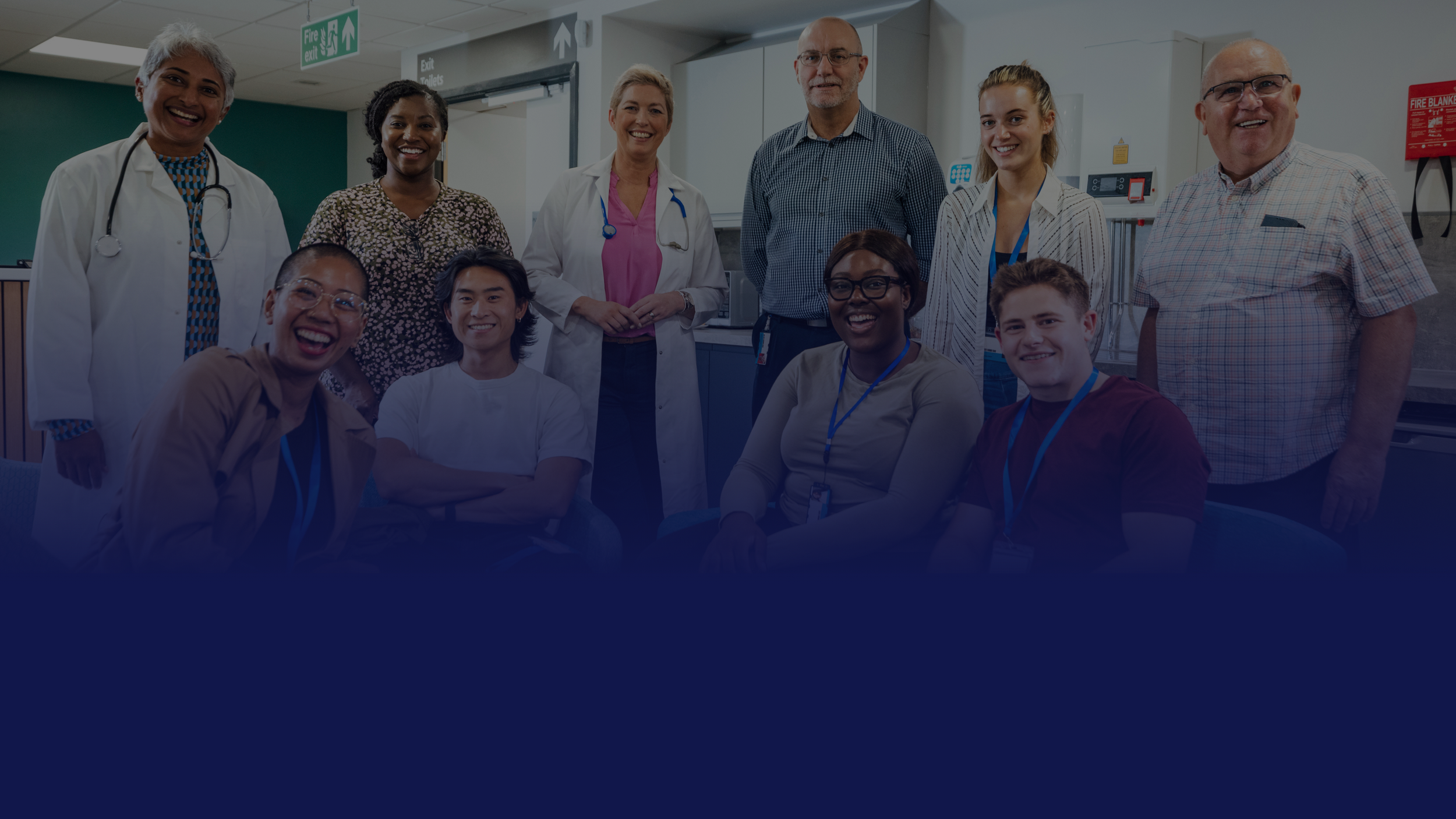 Group of healthcare professionals and staff standing together and smiling in a clinical setting, representing a collaborative senior care team.