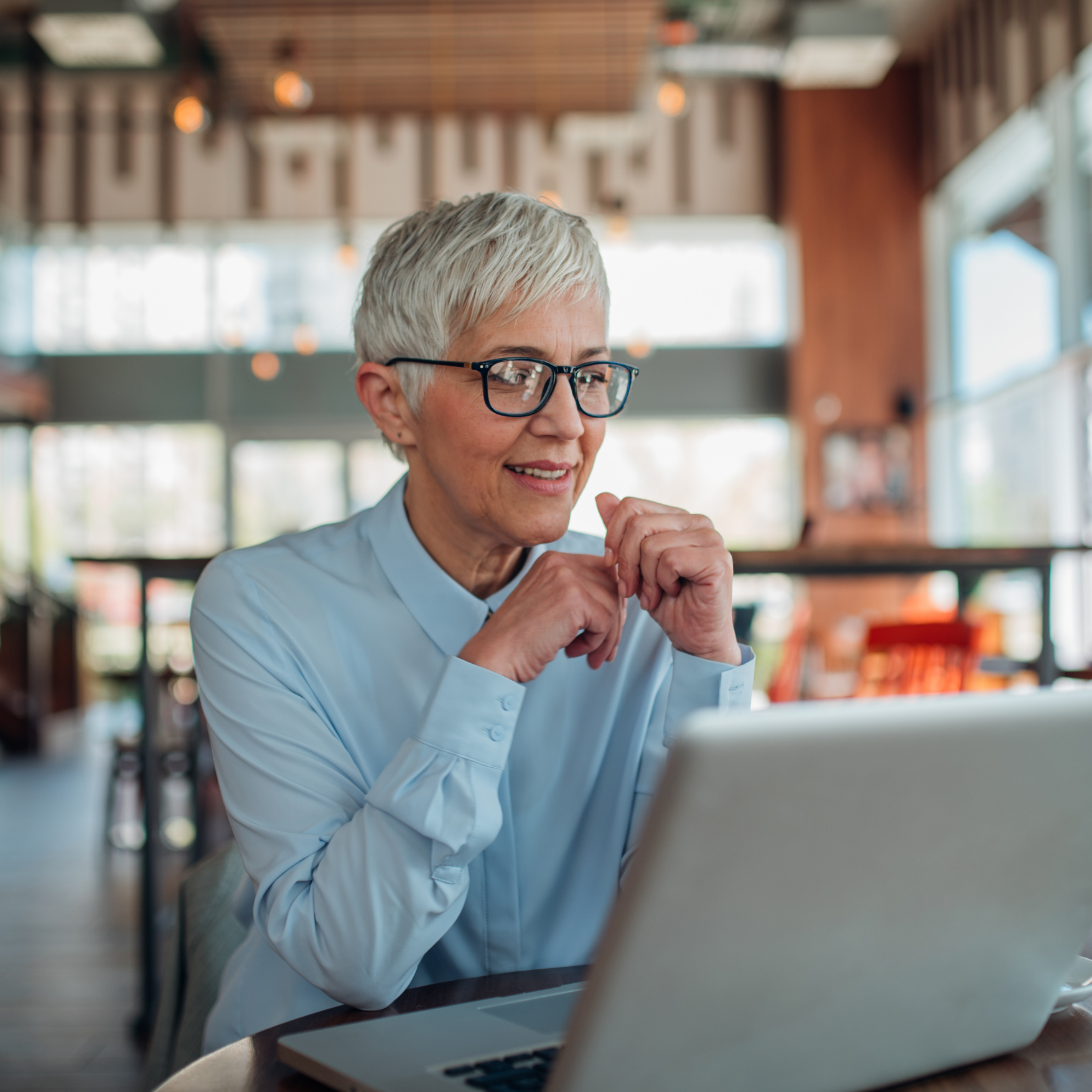 Older healthcare compliance professional with short gray hair and glasses working on a laptop for accreditation consulting.