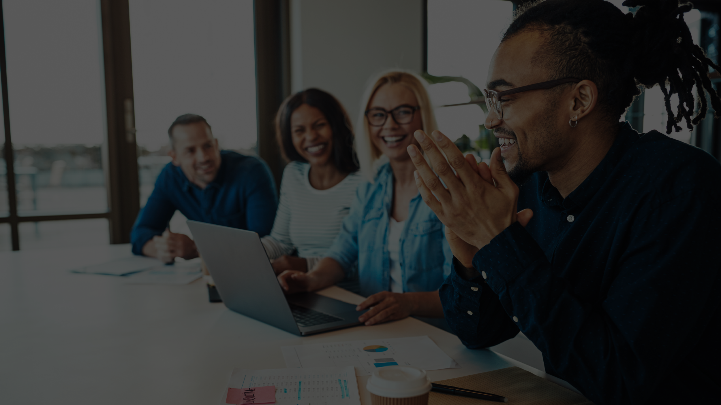 Group of diverse professionals collaborating around a laptop in a modern office setting, representing teamwork and compliance support in senior living.