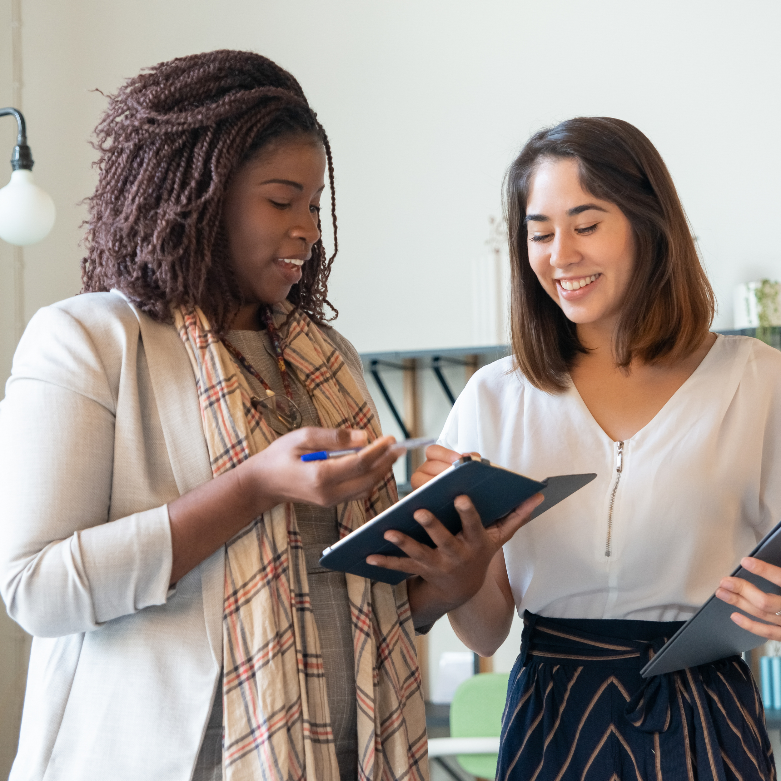 Two professionals standing together in an office, smiling and reviewing information on tablets while discussing quality improvement in senior living.
