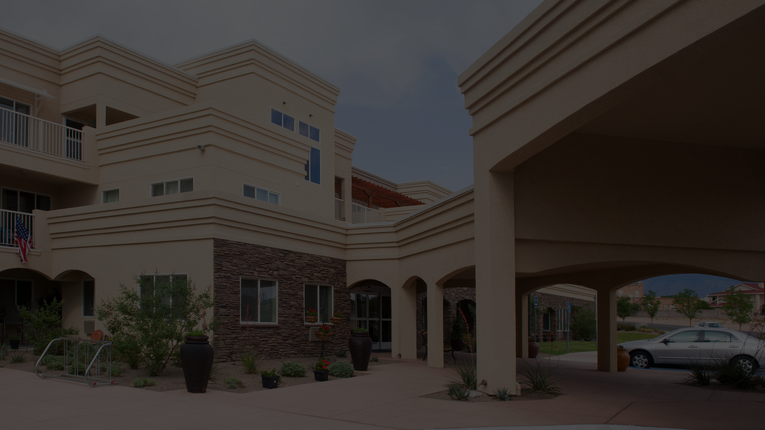 Exterior of a modern institutional building with arched entryways, stone and stucco facade, landscaped grounds, and a covered driveway in front.