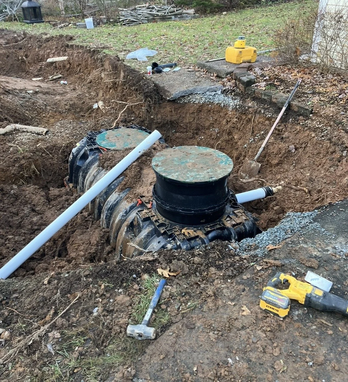 Installation of underground utility access pipes in a large excavated trench, with construction tools and materials nearby.