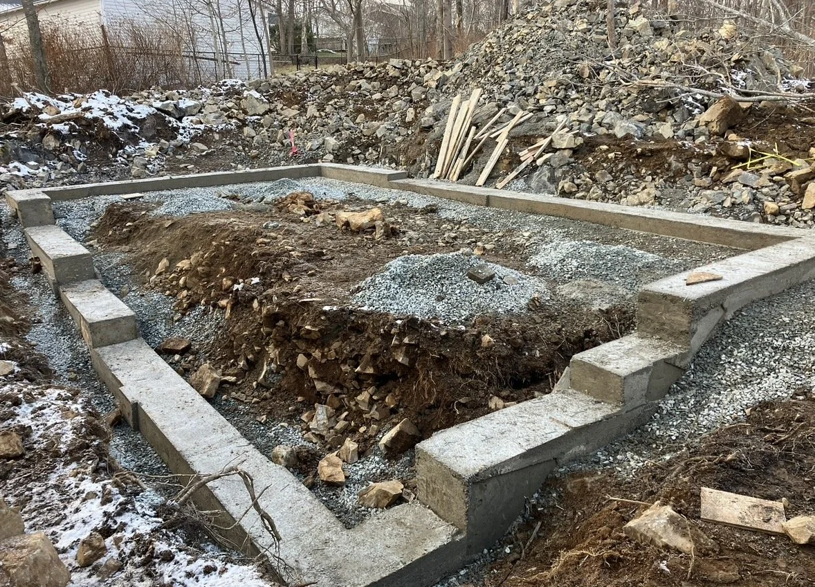 Construction site with a foundation being built, featuring concrete blocks and gravel, surrounded by dirt and rocks.