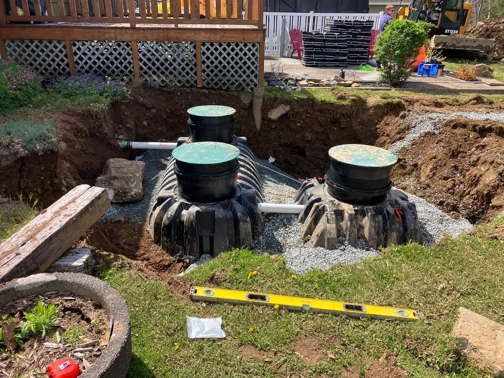Three septic tanks installed in a backyard excavation site, surrounded by soil and construction materials.