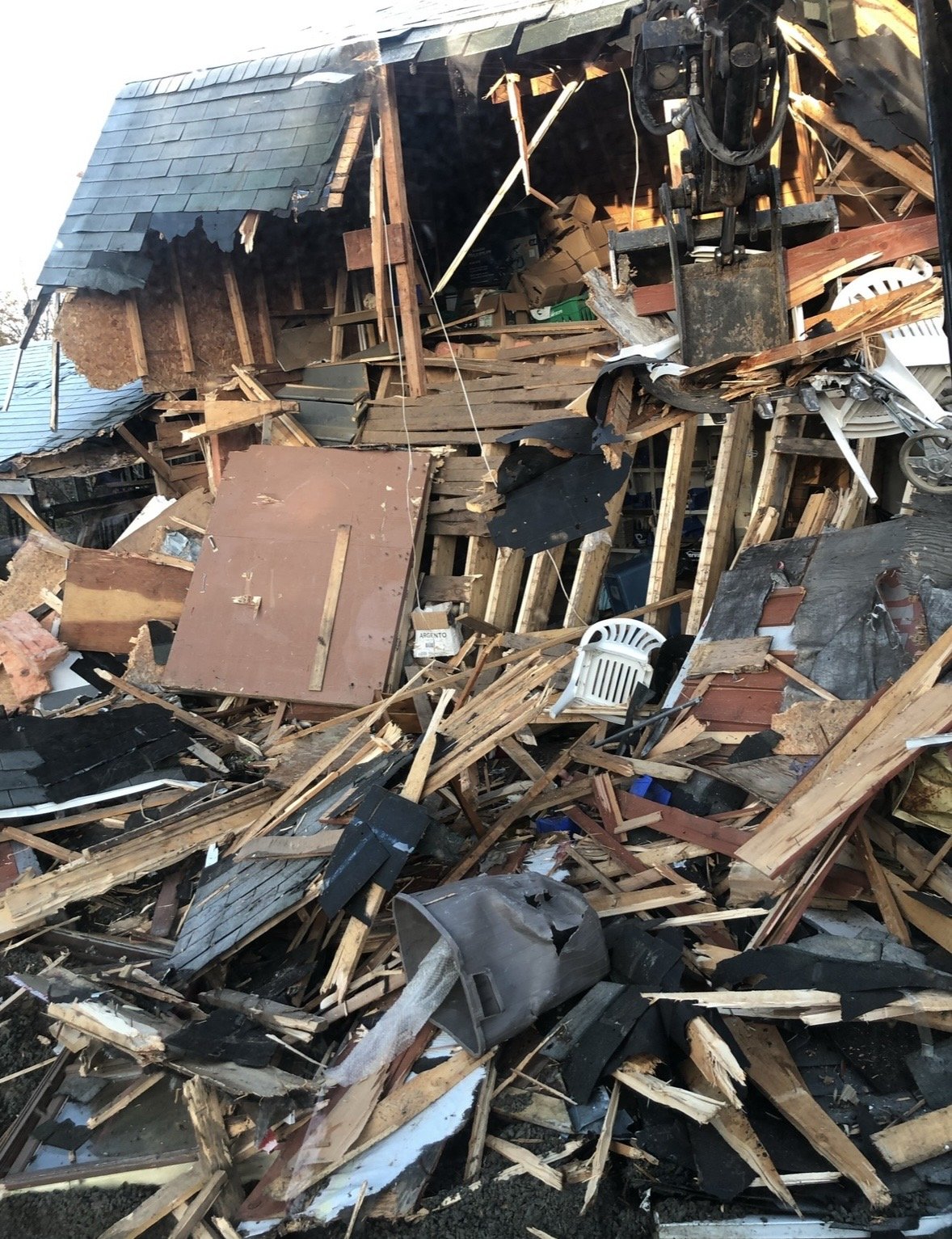 Debris and wreckage of a house destroyed by a disaster with wooden beams, shattered roofing, and scattered household items.