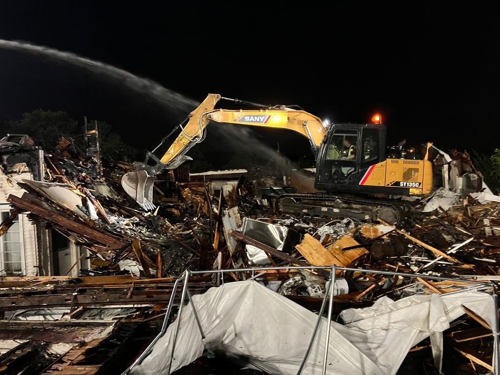 A yellow excavator clearing debris from a collapsed building at night.