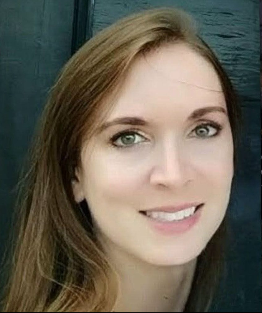 Close-up of a woman with long brown hair and light-colored eyes smiling at the camera.
