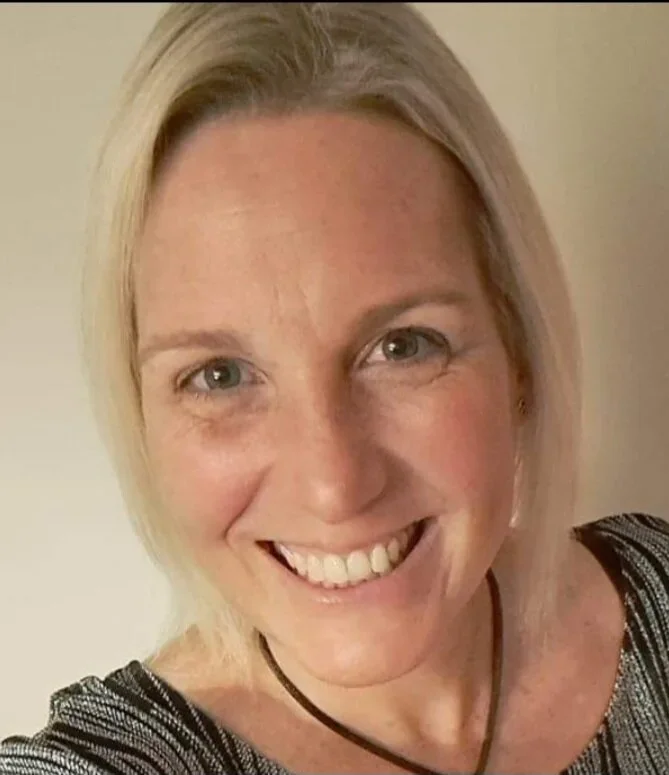 Close-up of a smiling woman with blonde hair and blue eyes wearing a black and white striped top.