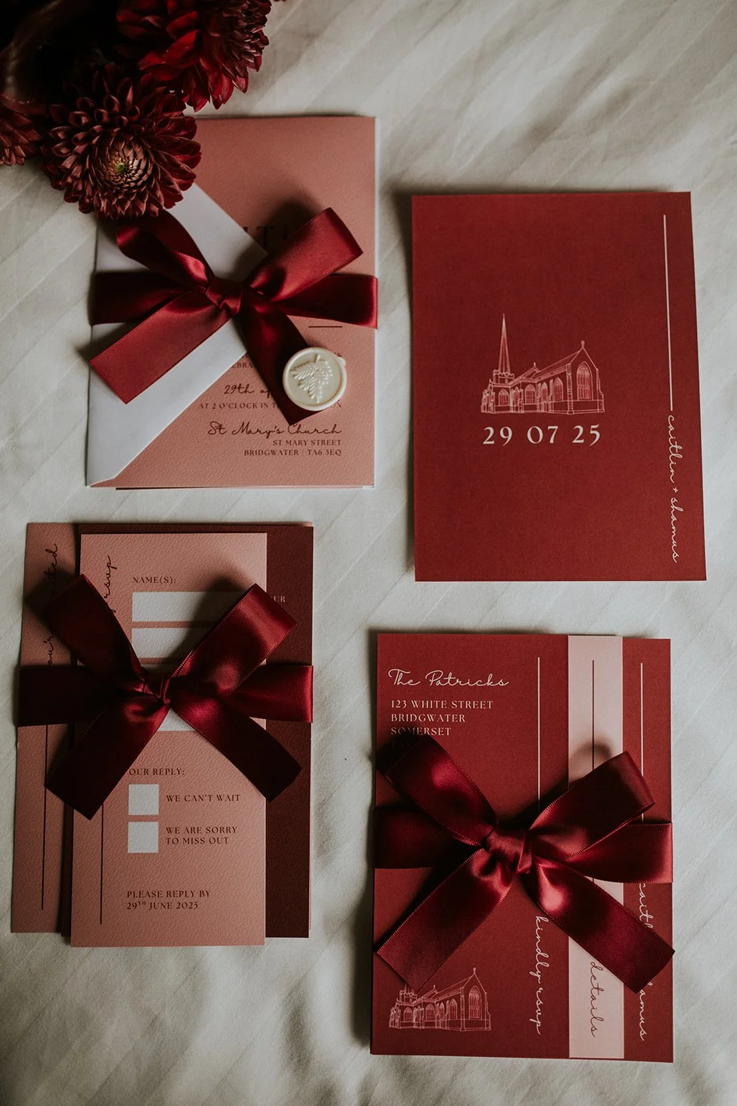 Flatlay of wedding invitation suite featuring layered cards, satin bow and venue illustration