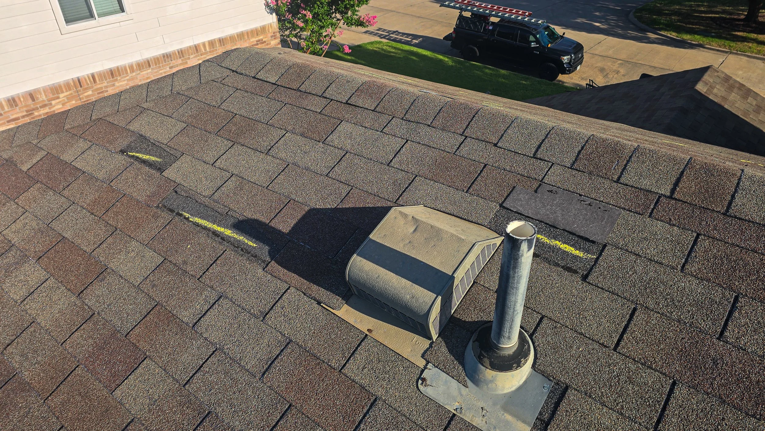 Close-up of a roof with brown asphalt shingles, with yellow chalk markings indicating measurements and notes for roof repair, including numbers, letters, and arrows. Roof Inspection.