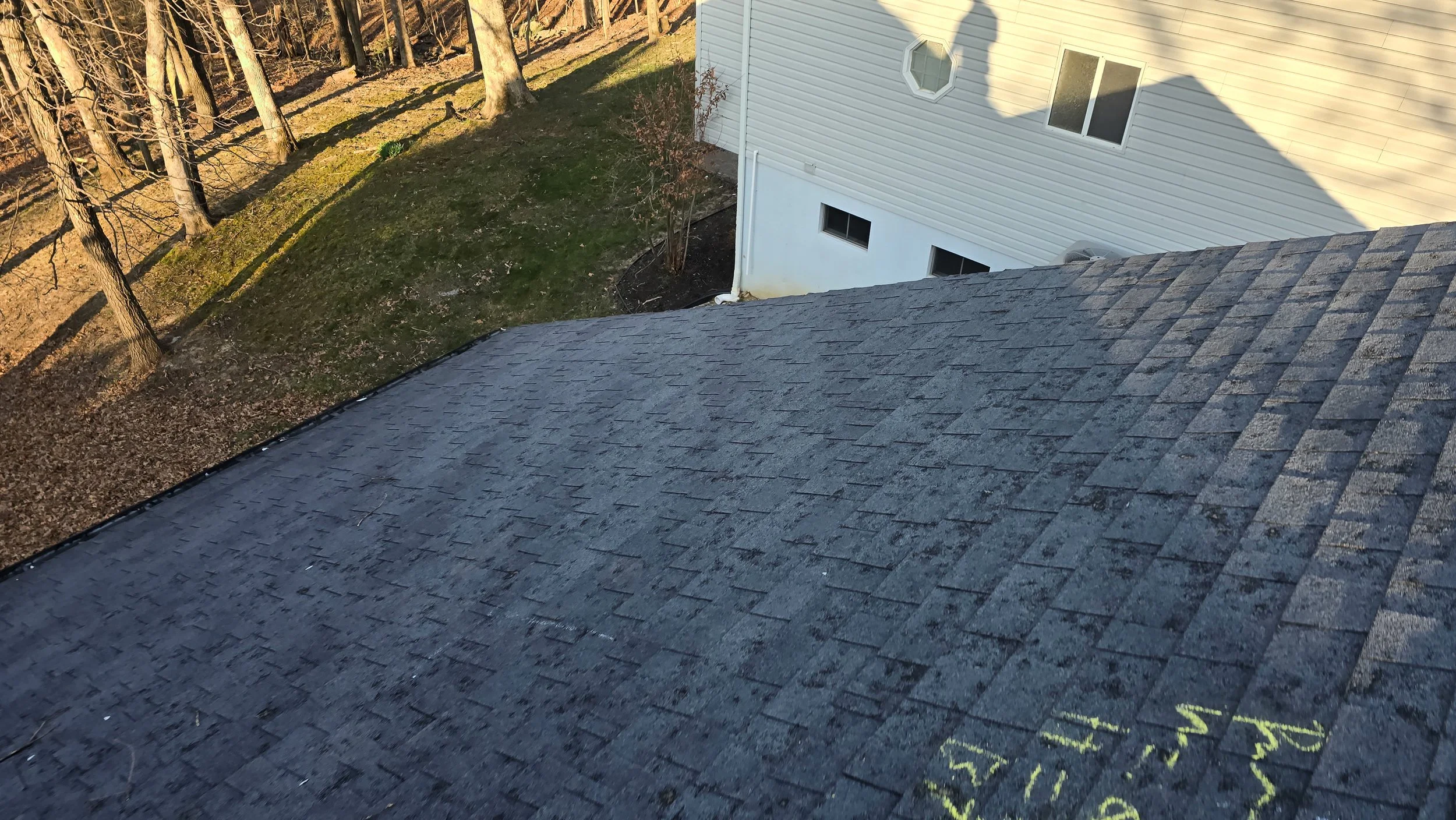 Close-up of a roof with brown asphalt shingles, with yellow chalk markings indicating measurements and notes for roof repair, including numbers, letters, and arrows. Roof Inspection.