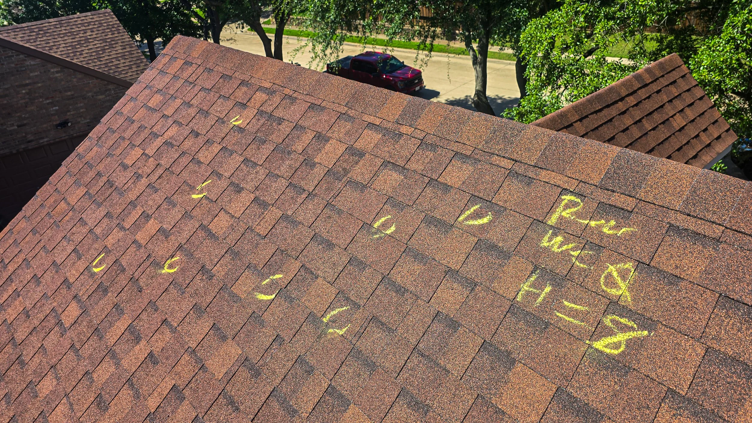Close-up of a roof with brown asphalt shingles, with yellow chalk markings indicating measurements and notes for roof repair, including numbers, letters, and arrows. Roof Inspection.