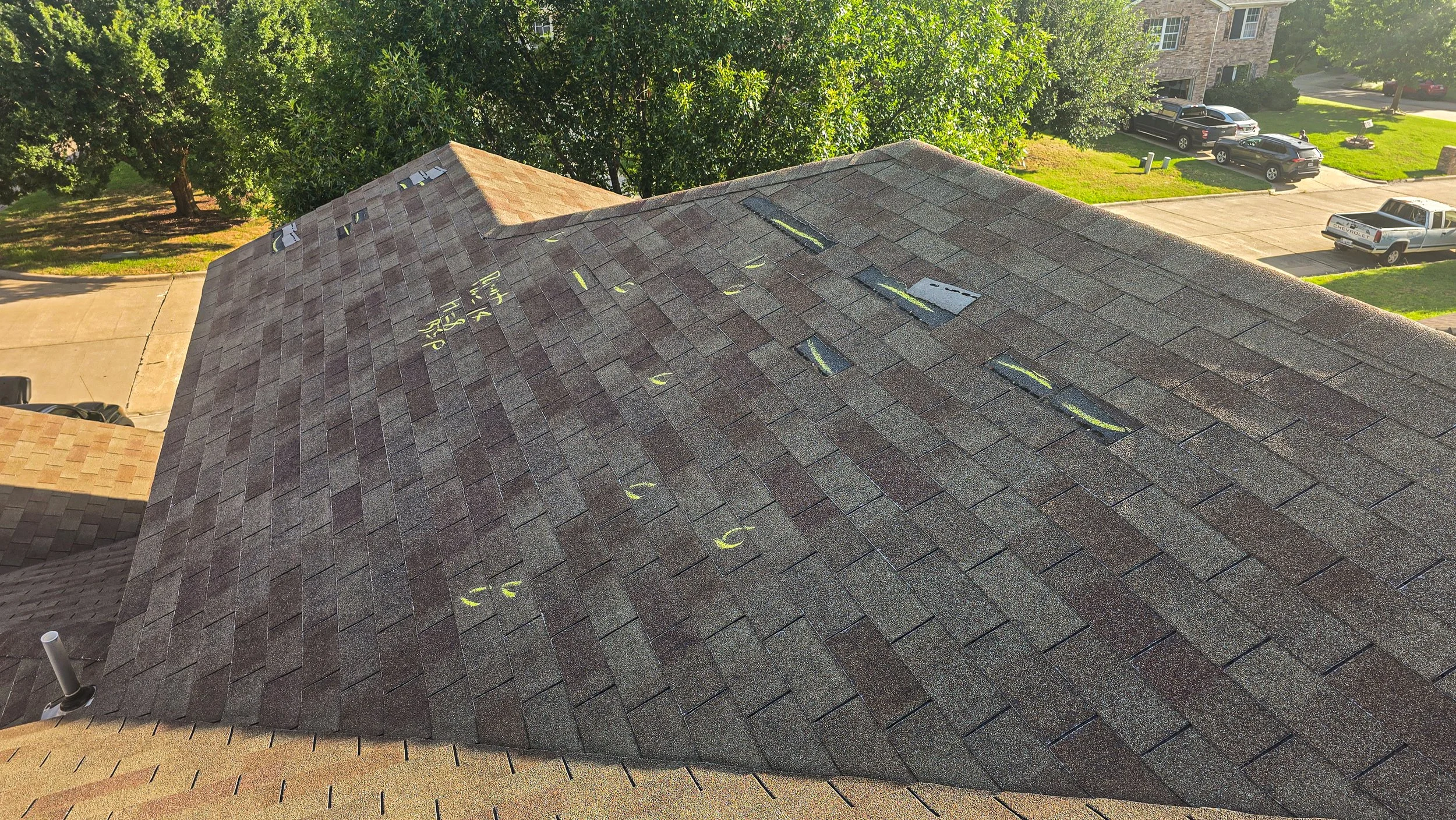 Close-up of a roof with brown asphalt shingles, with yellow chalk markings indicating measurements and notes for roof repair, including numbers, letters, and arrows. Roof Inspection.