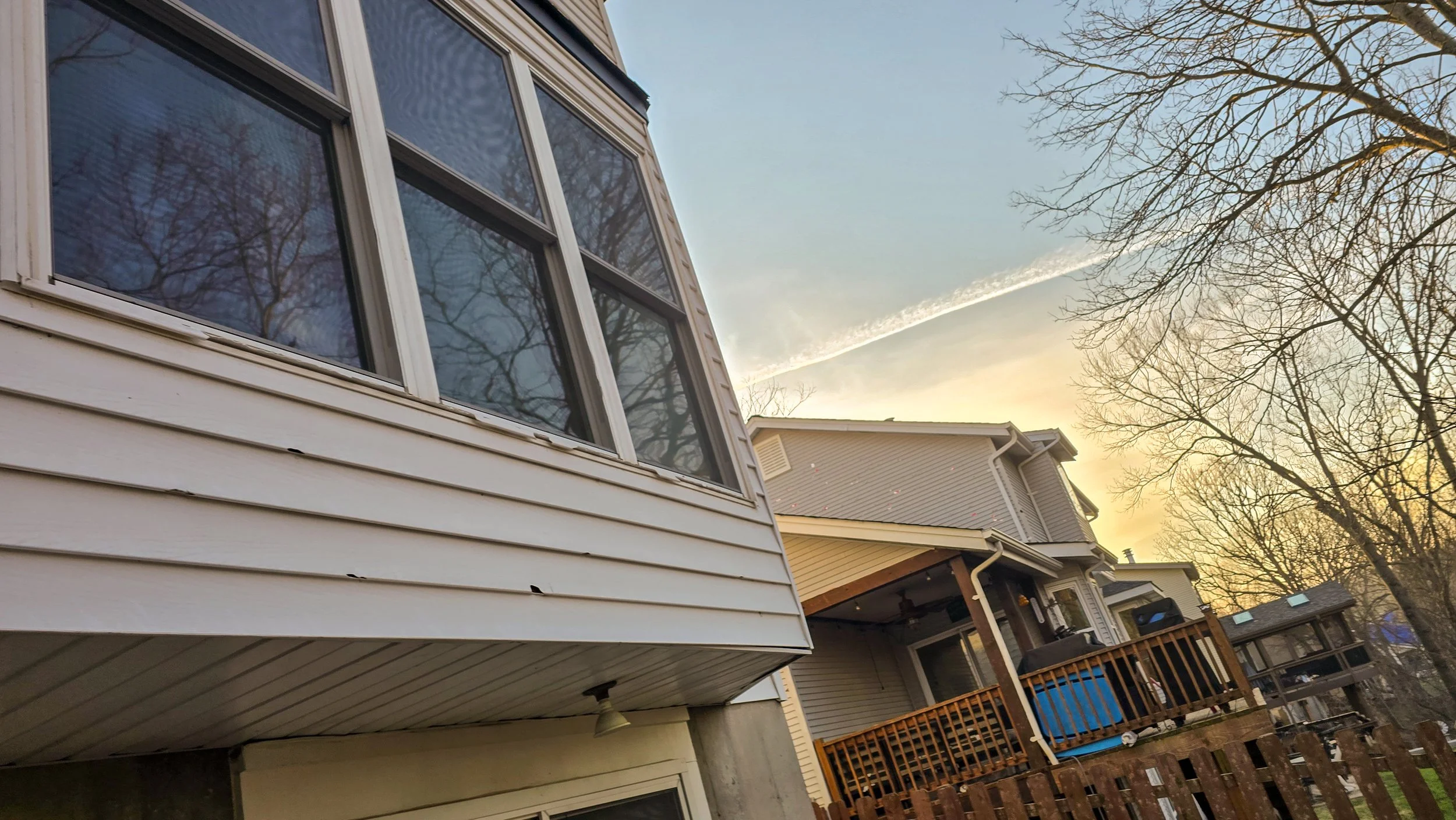 A residential neighborhood during sunset showing the exterior of houses with decks and trees without leaves in the background.