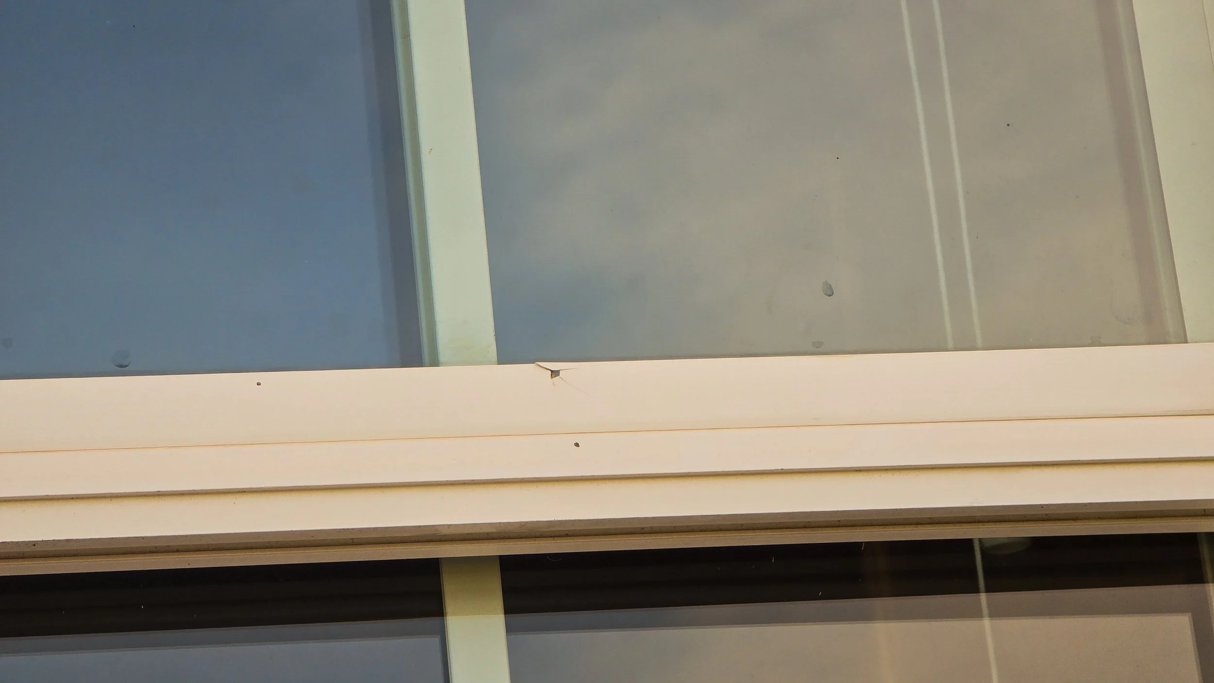 Close-up of a window with a damaged or cracked white frame, showing some dirt and small marks.