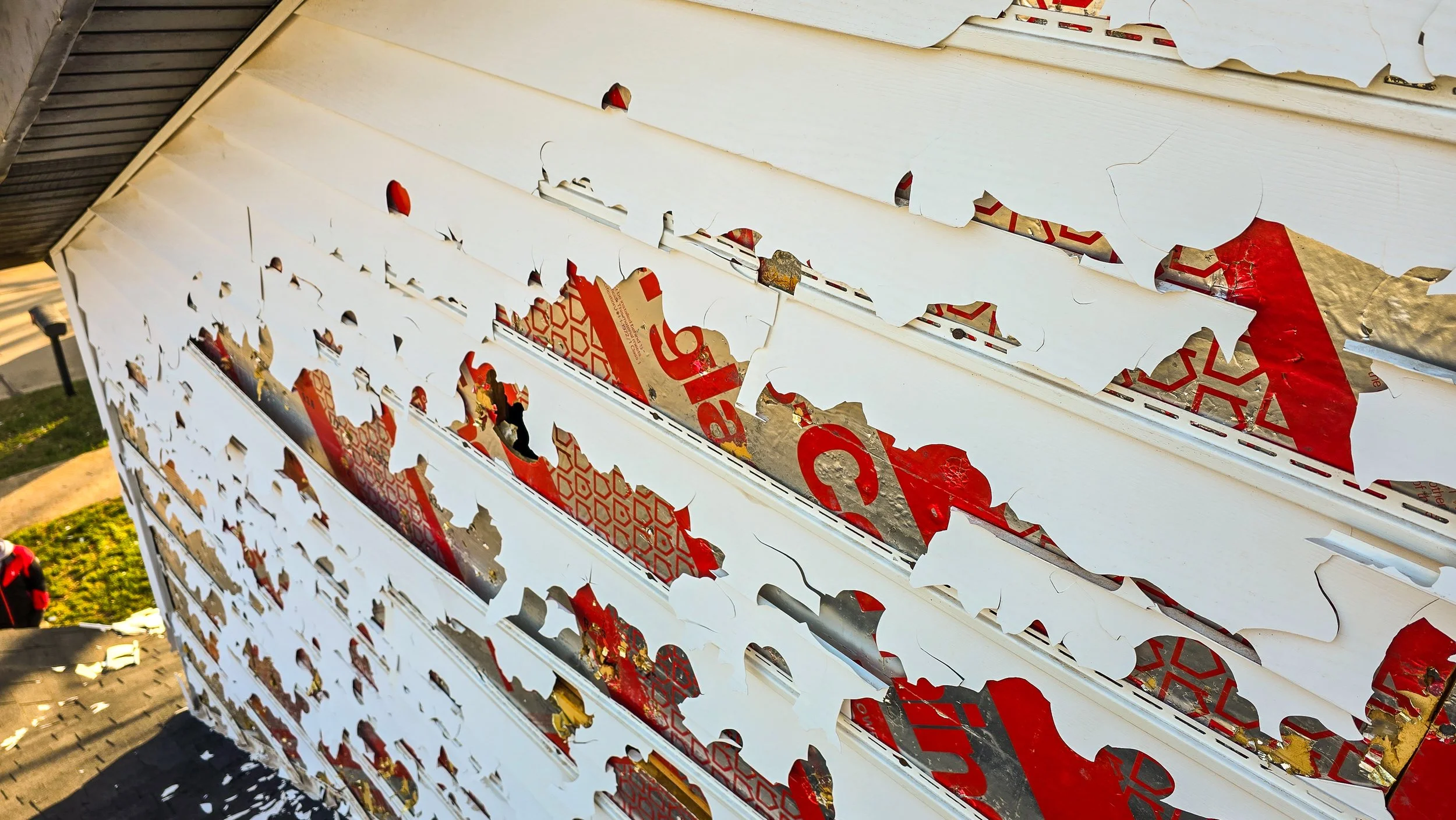 Close-up of a white, torn, and damaged billboard or sign with parts of red and gold paper or stickers underneath.