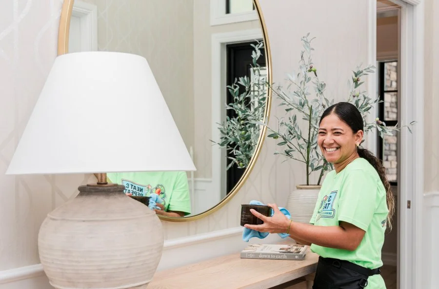 Neat and Repeat Cleaning technician dusting a mirror and console table in a home