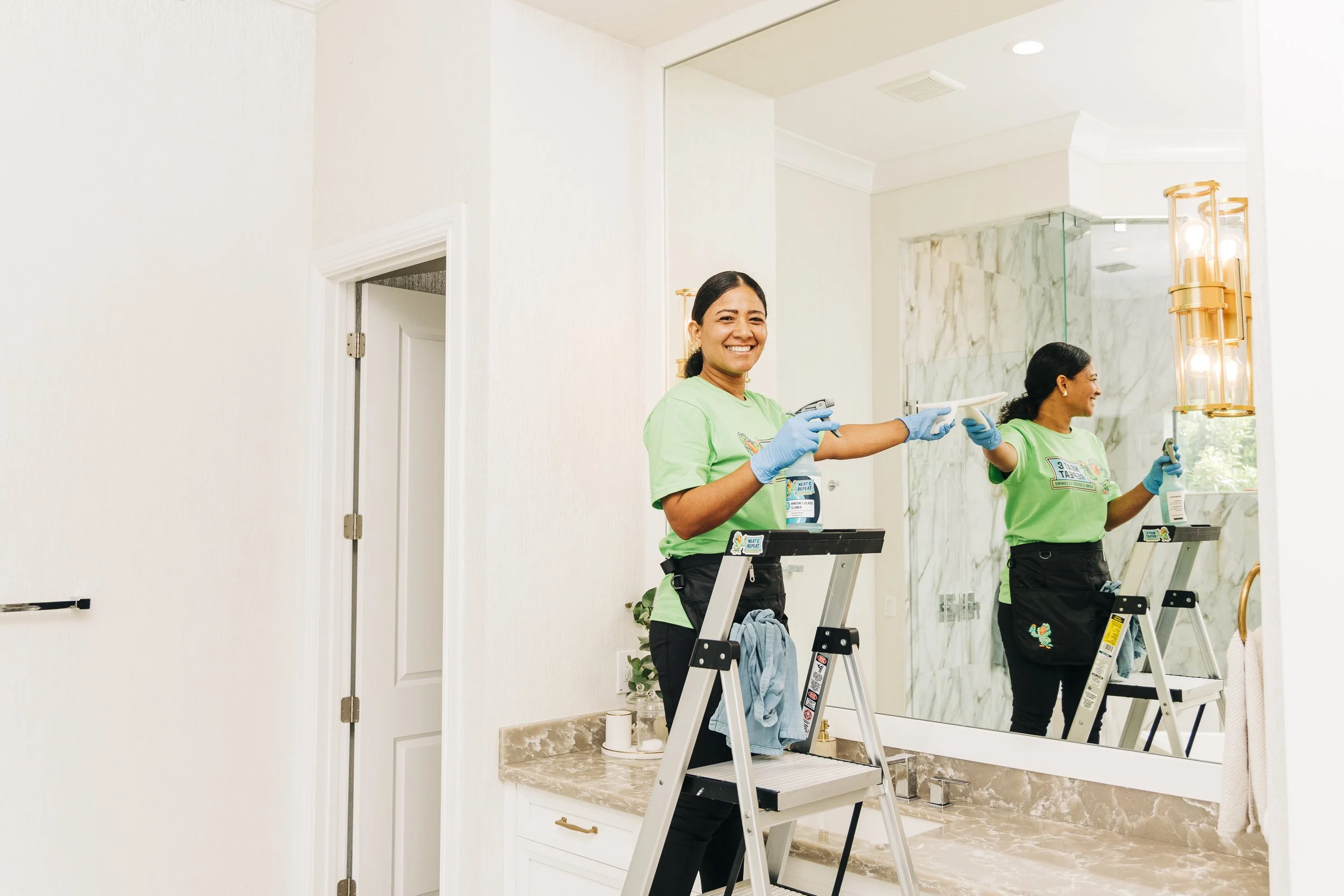 Two Neat and Repeat Cleaning technicians cleaning a bathroom mirror and vanity