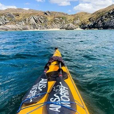 Yellow kayak on clear blue water with rocky hills and cloudy sky in background.
