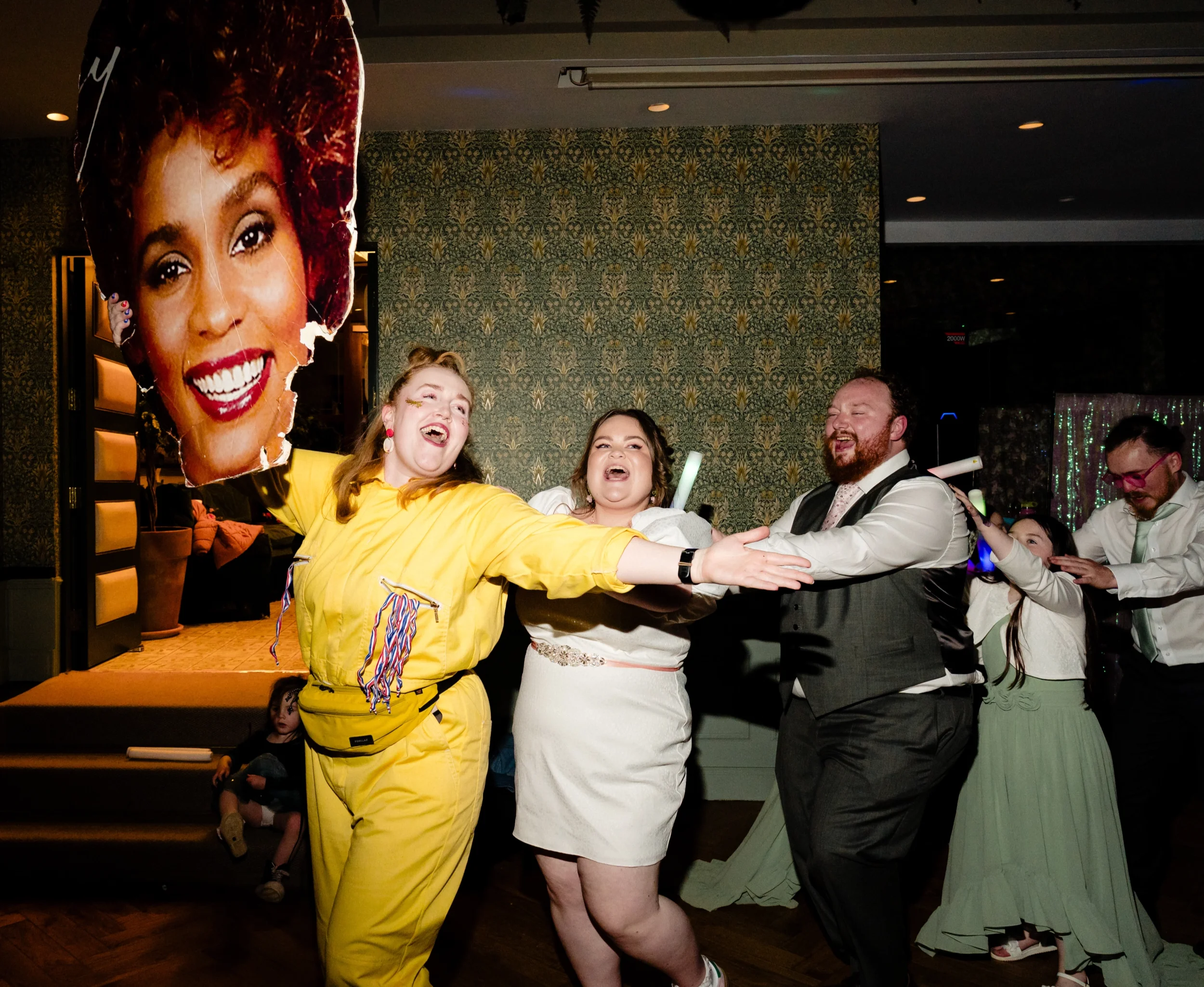 People enjoying a dance at a celebration, with a woman holding a large photo of a smiling woman as a decoration.