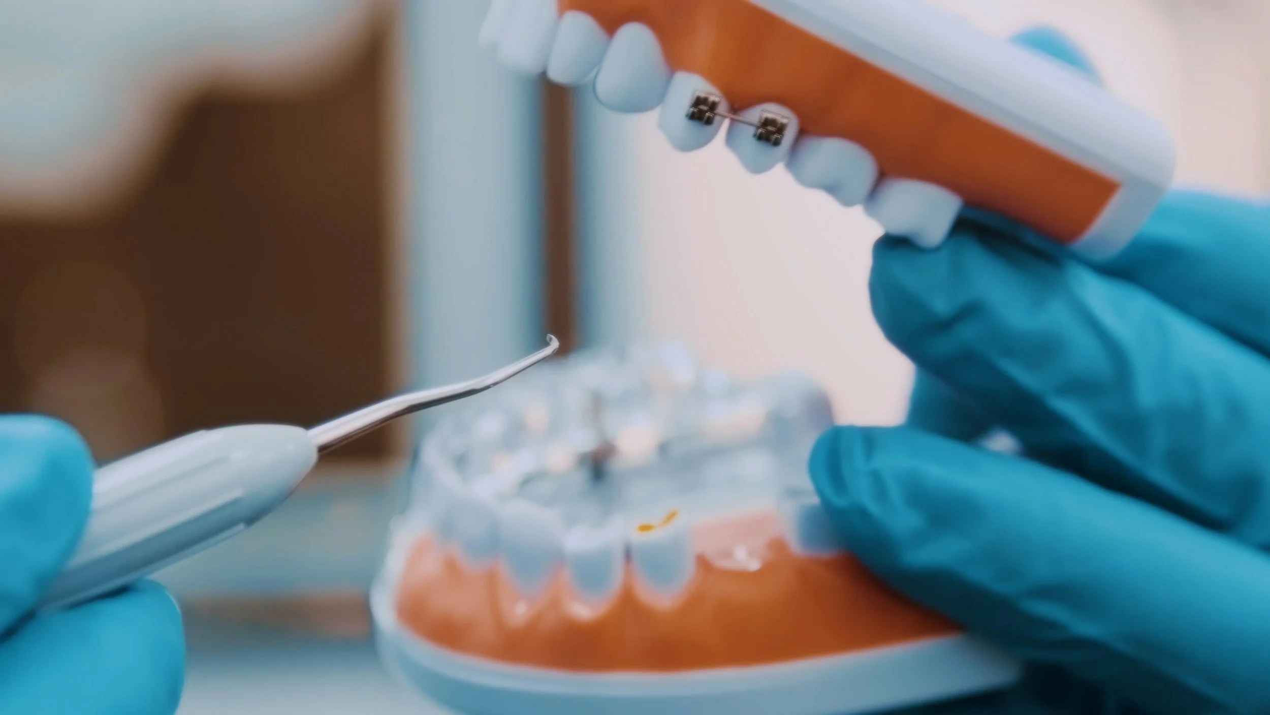 Close-up of a dentist or dental technician working on a dental model with orthodontic braces, using a precision tool, while wearing blue latex gloves.
