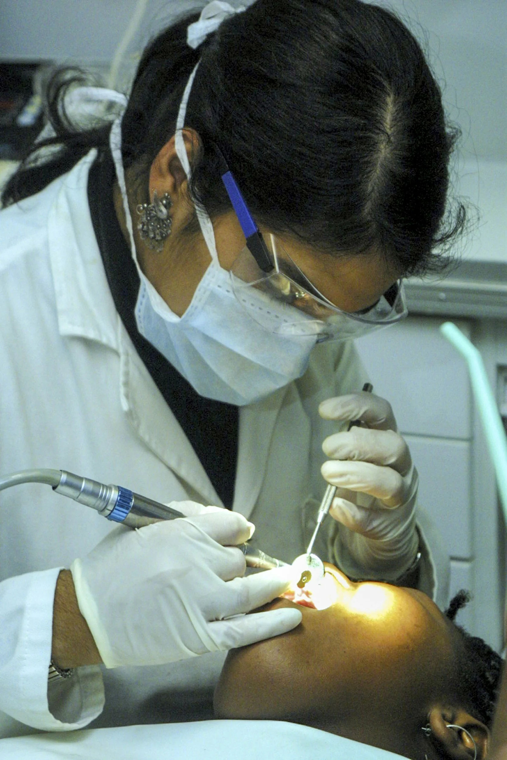 A dentist wearing gloves and a face mask performs dental work on a patient in a dental clinic.