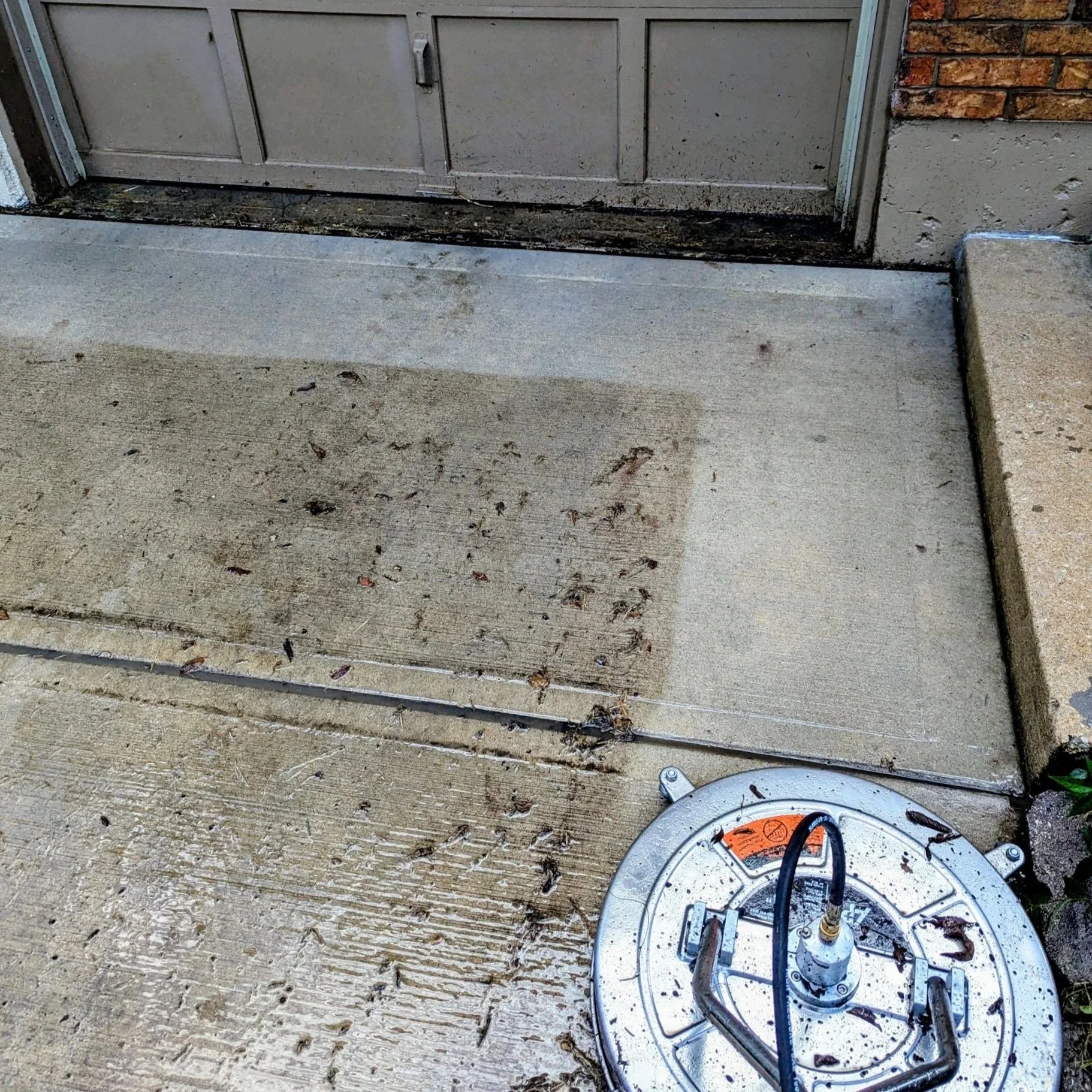 Concrete porch with a door and a sidewalk, with a round metal device on the ground near a step, surrounded by dirt and small debris.