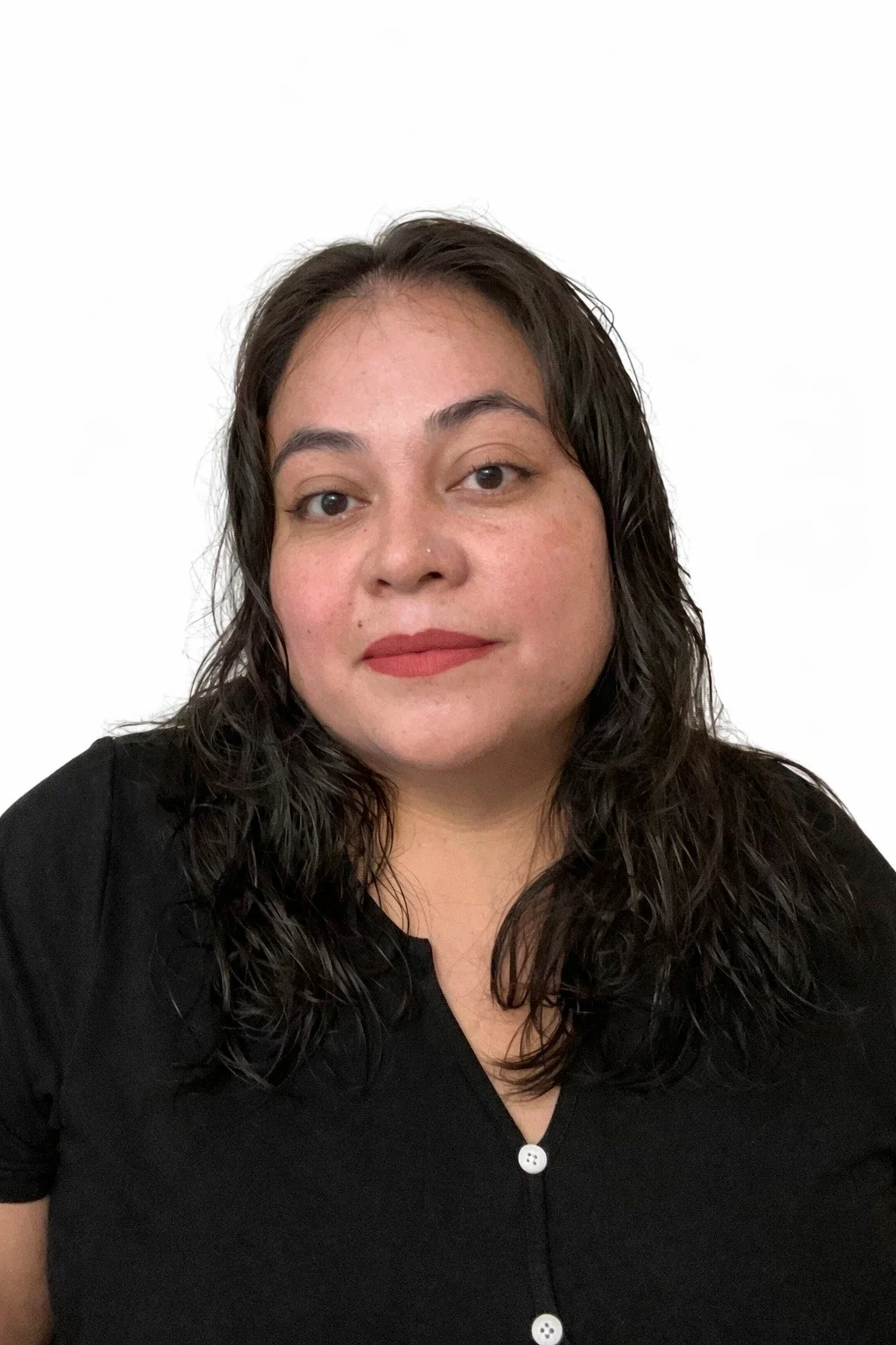 A woman with dark, curly hair wearing a black shirt with white buttons, looking at the camera against a plain white background.