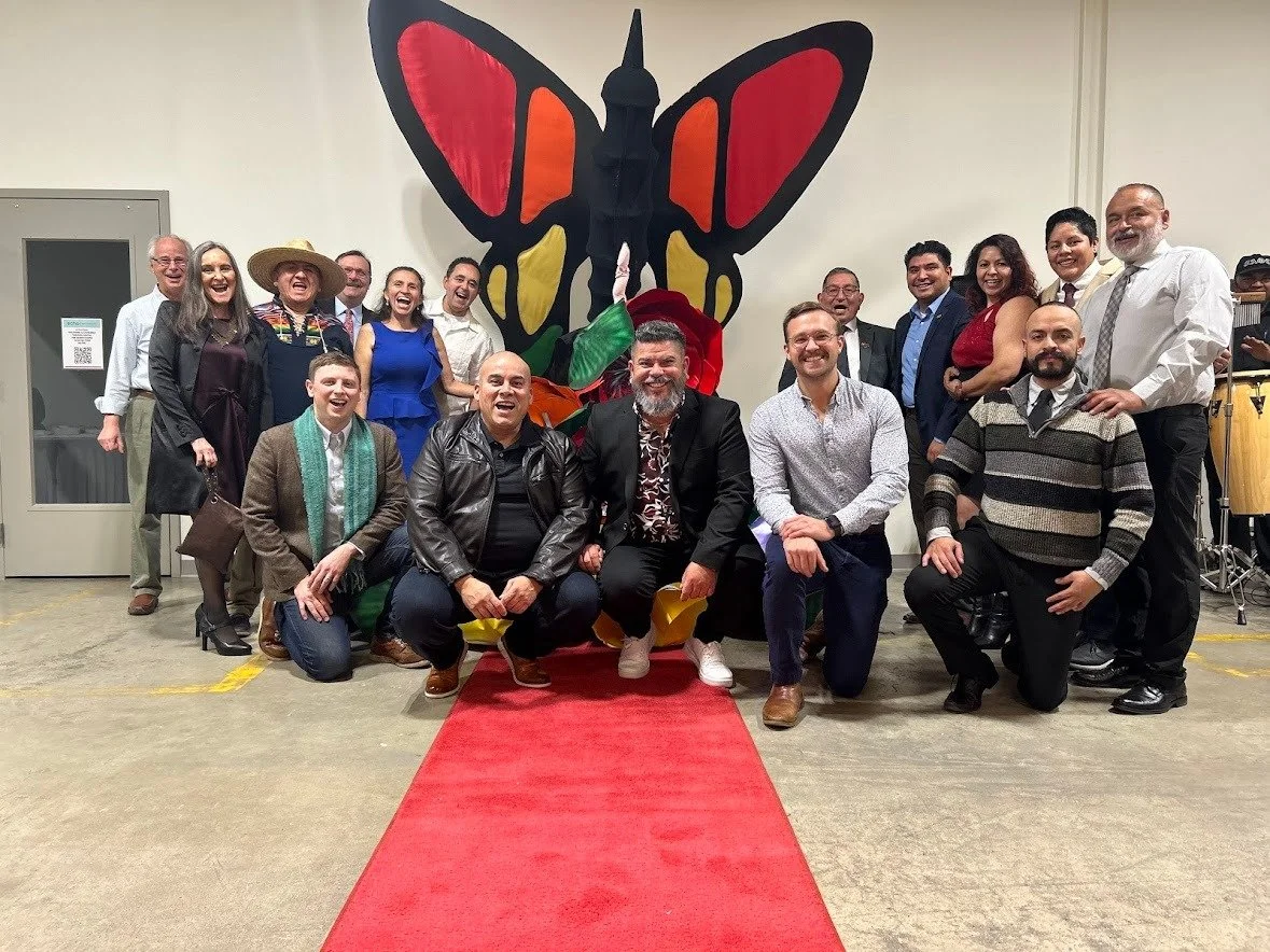 Group of people posing for photo in front of colorful butterfly artwork on wall, with red carpet on floor.
