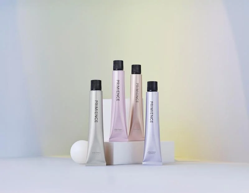 Four priming skincare tubes in pastel colors arranged on white blocks against a gradient background.
