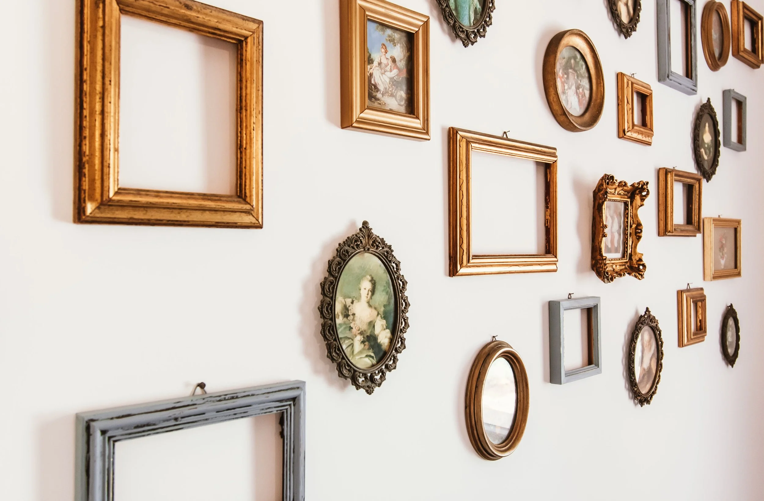 A wall decorated with various empty picture frames and vintage-style framed photographs arranged in a collage.