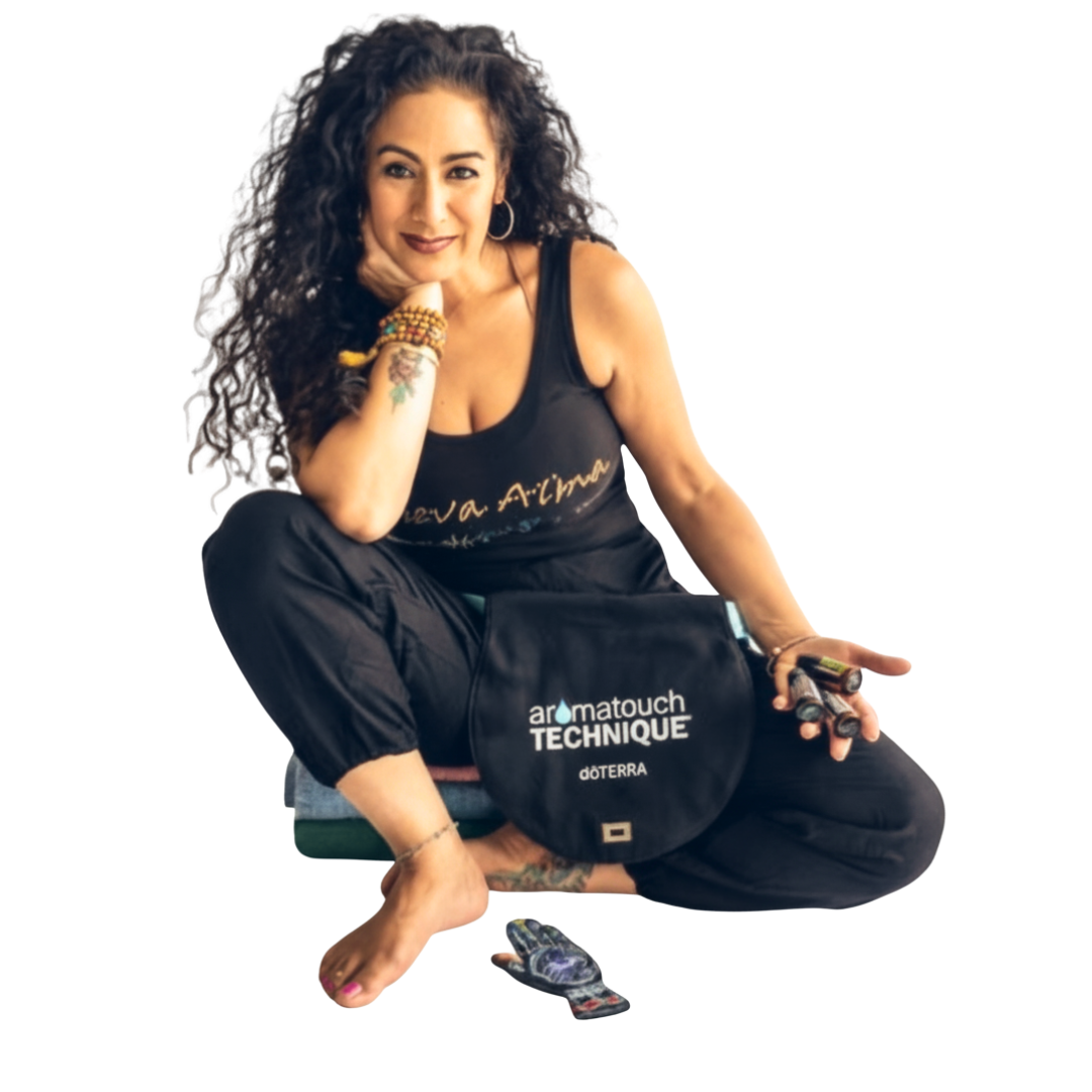 A woman with curly dark hair, tattoos, and jewelry sitting in a cross-legged pose, holding a small object in one hand, with a bag labeled Gotermateouch Technique and doTERRA in front of her.