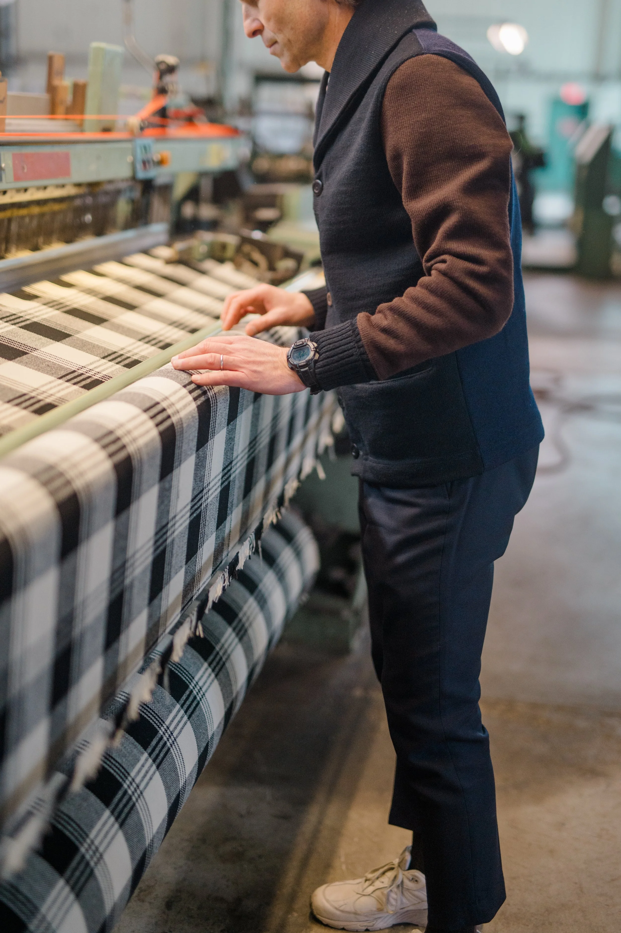 A person inspecting plaid fabric on a textile machine in a factory.