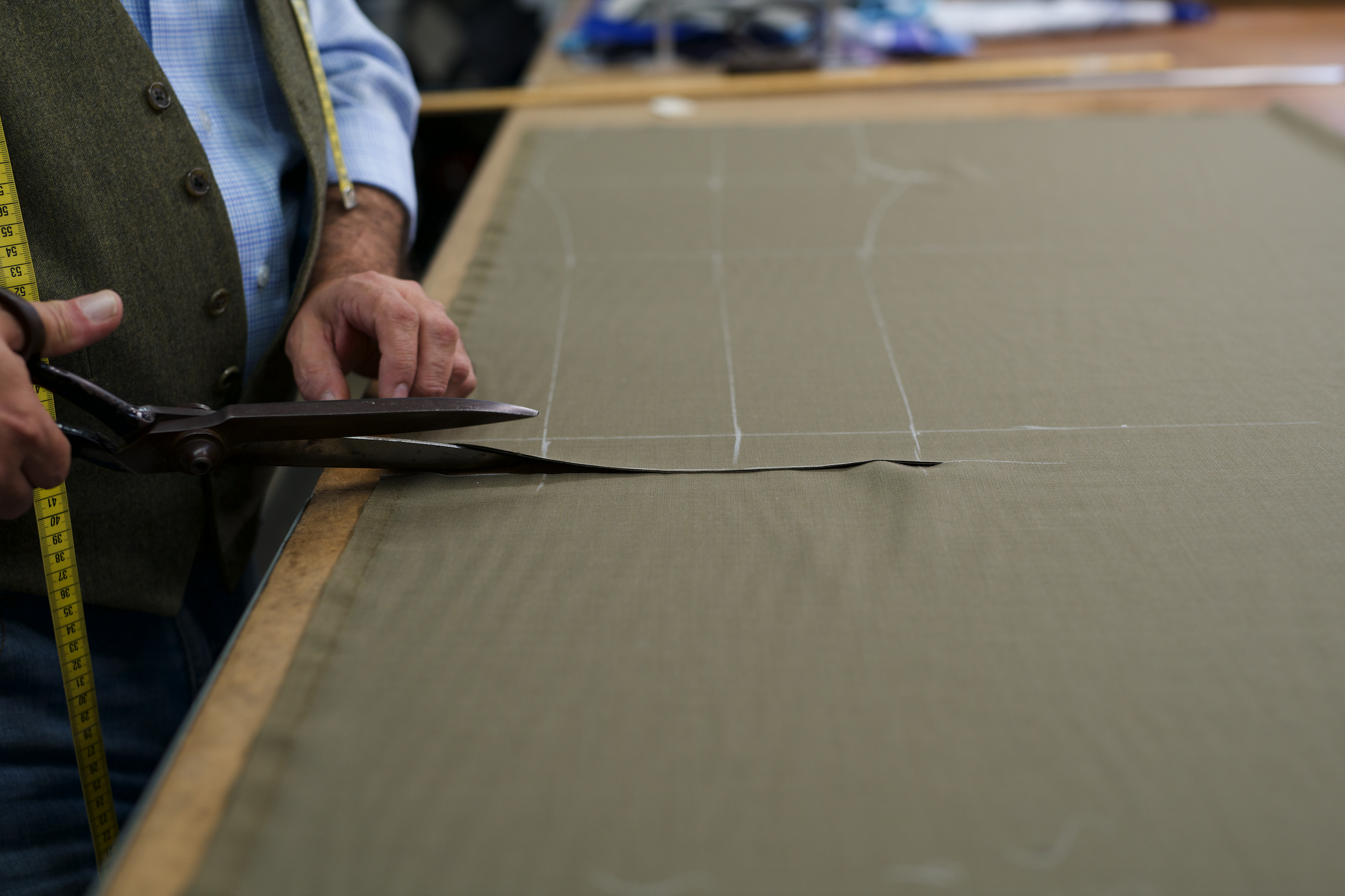 A person is cutting a piece of fabric with scissors on a worktable, with fabric measuring markings visible.