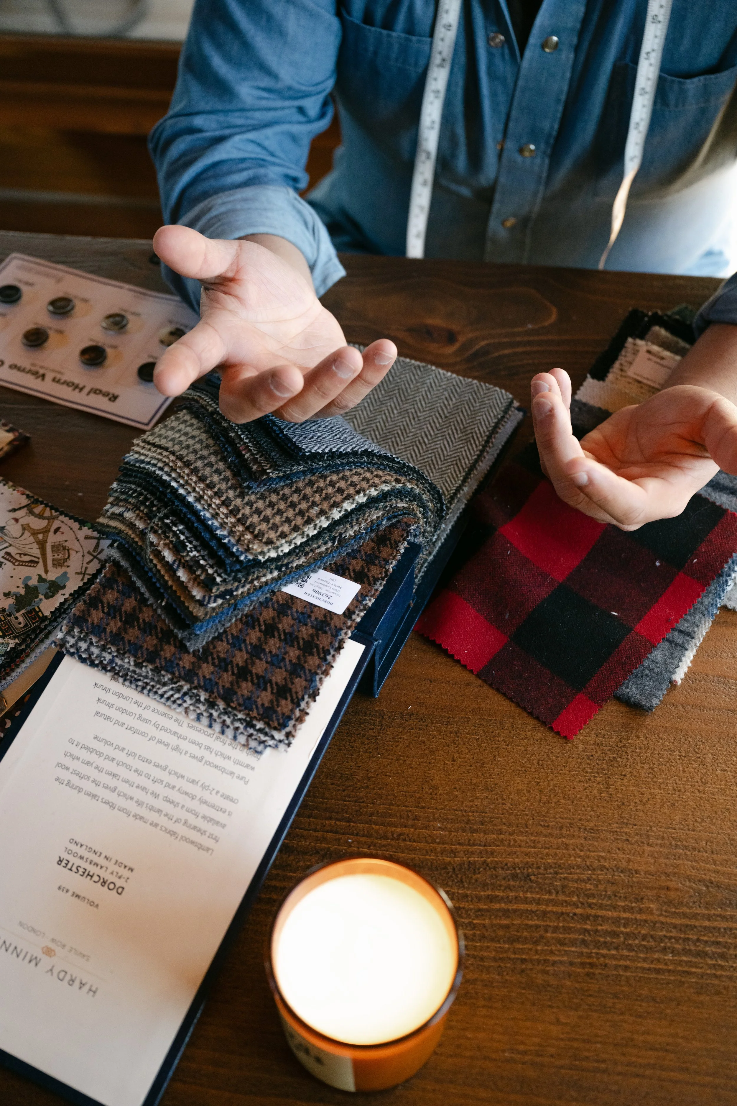 Person displaying fabric swatches and discussing clothing options at a table with fabric samples and sample books.