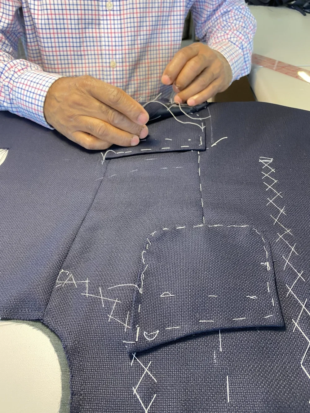 Person sewing fabric with markings and pattern outlines on dark fabric.