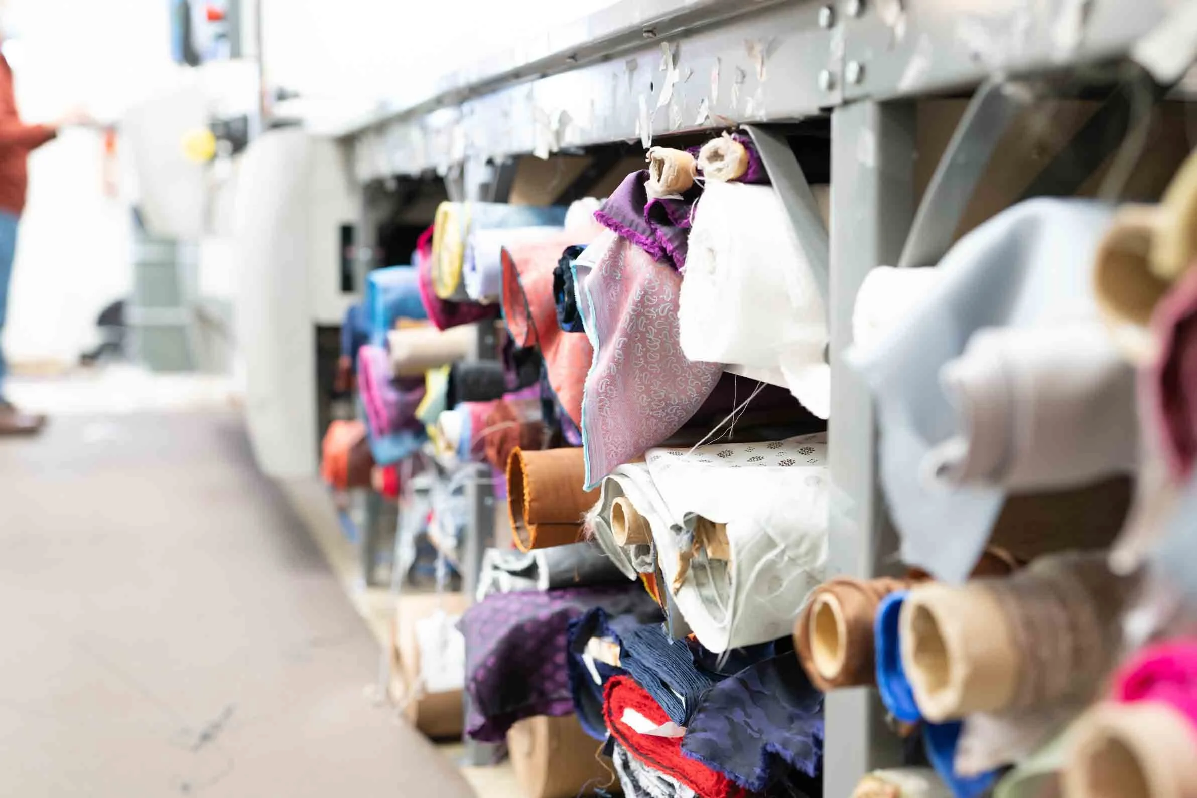 A variety of fabric rolls in different colors and patterns on a metal storage cart at a fabric store or workshop.