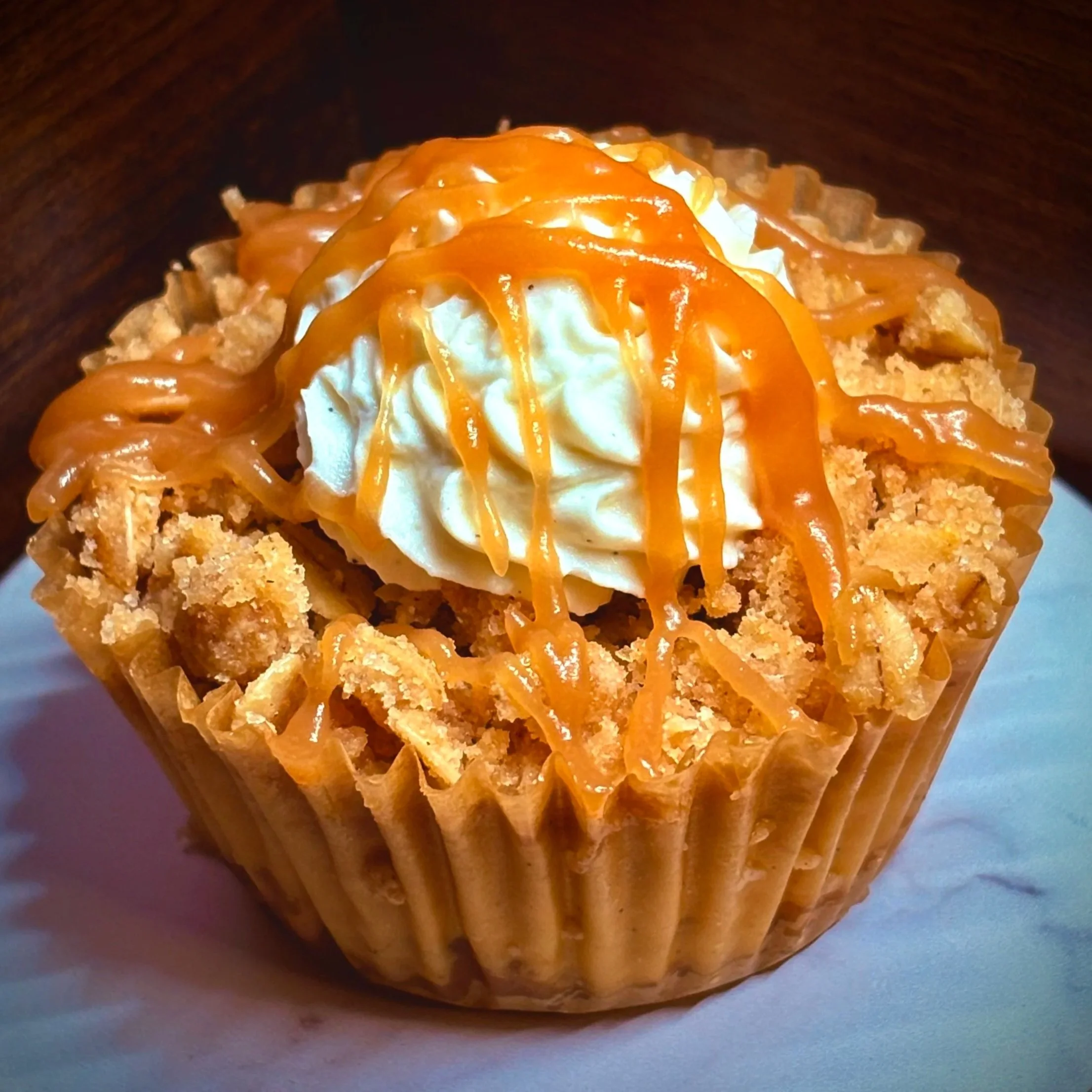 Cupcake topped with whipped cream and caramel drizzle on a white plate.